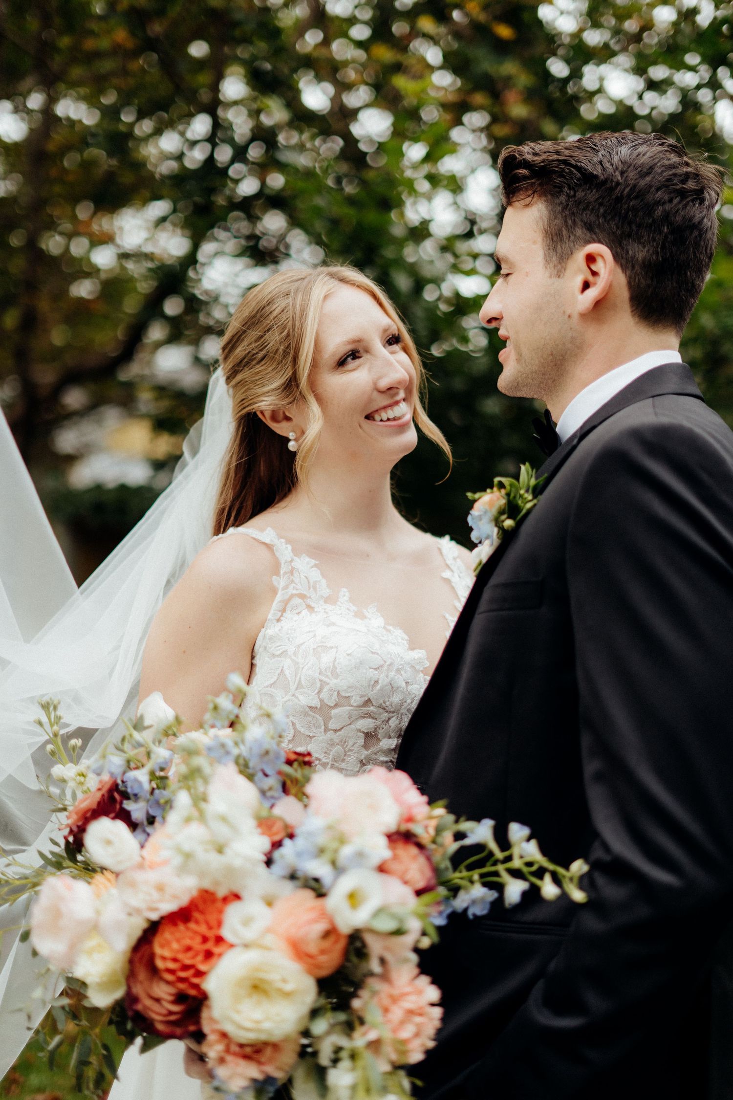 Elegant wedding portrait featuring coral and white floral bouquet in an outdoor garden setting.