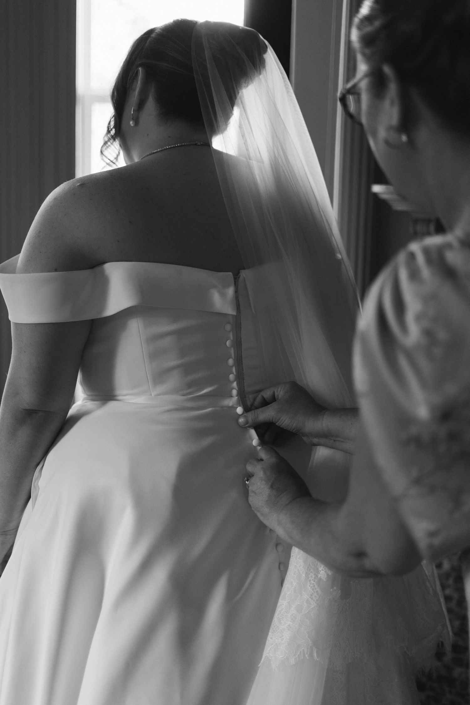 Close-up details of white wedding dress being adjusted in natural window light.