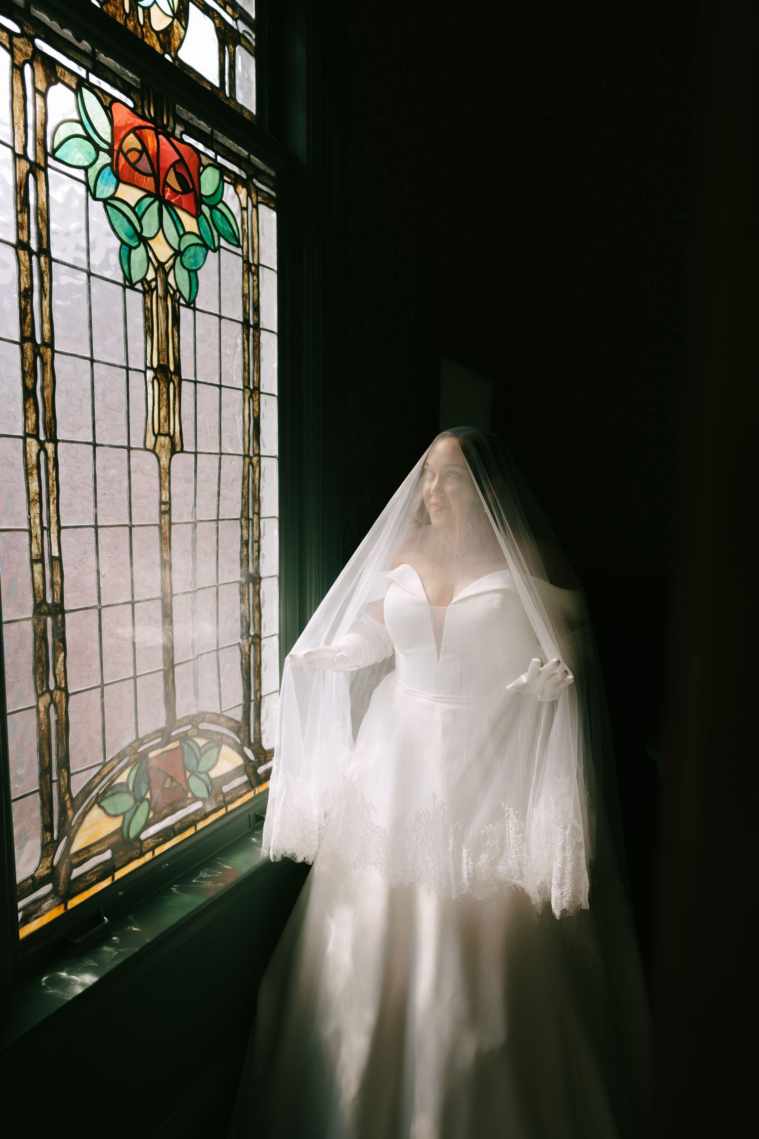 Wedding gown elegantly displayed against stained glass windows creating ethereal lighting effects.