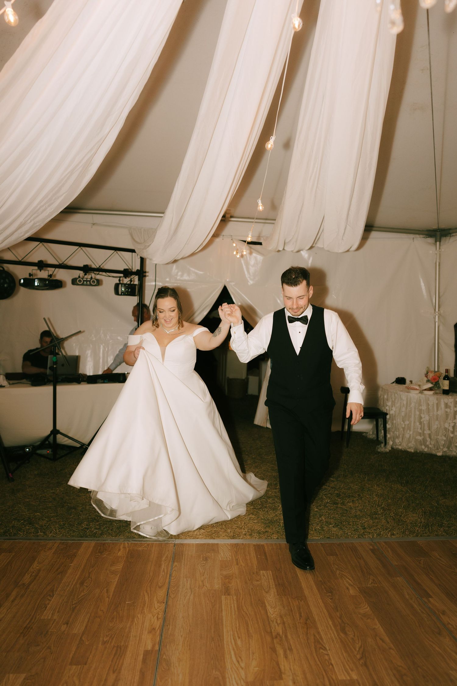 A couple performs a playful dance sequence in a white draped reception tent with wooden floors.