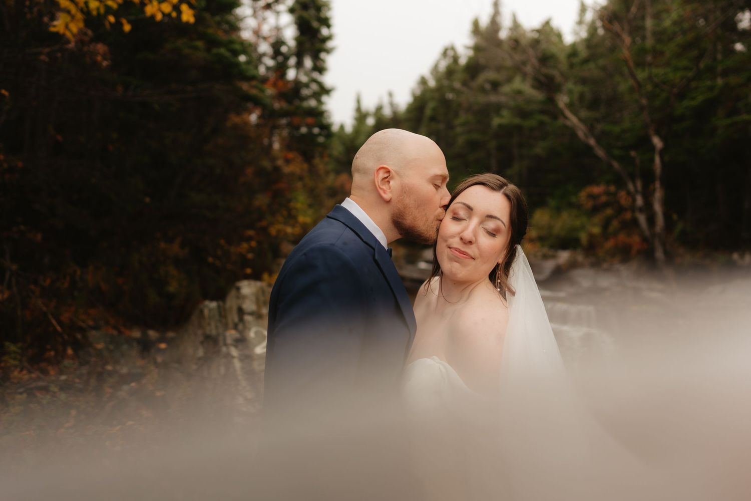 A romantic couple embraces during their outdoor autumn wedding photoshoot in a misty forest setting.