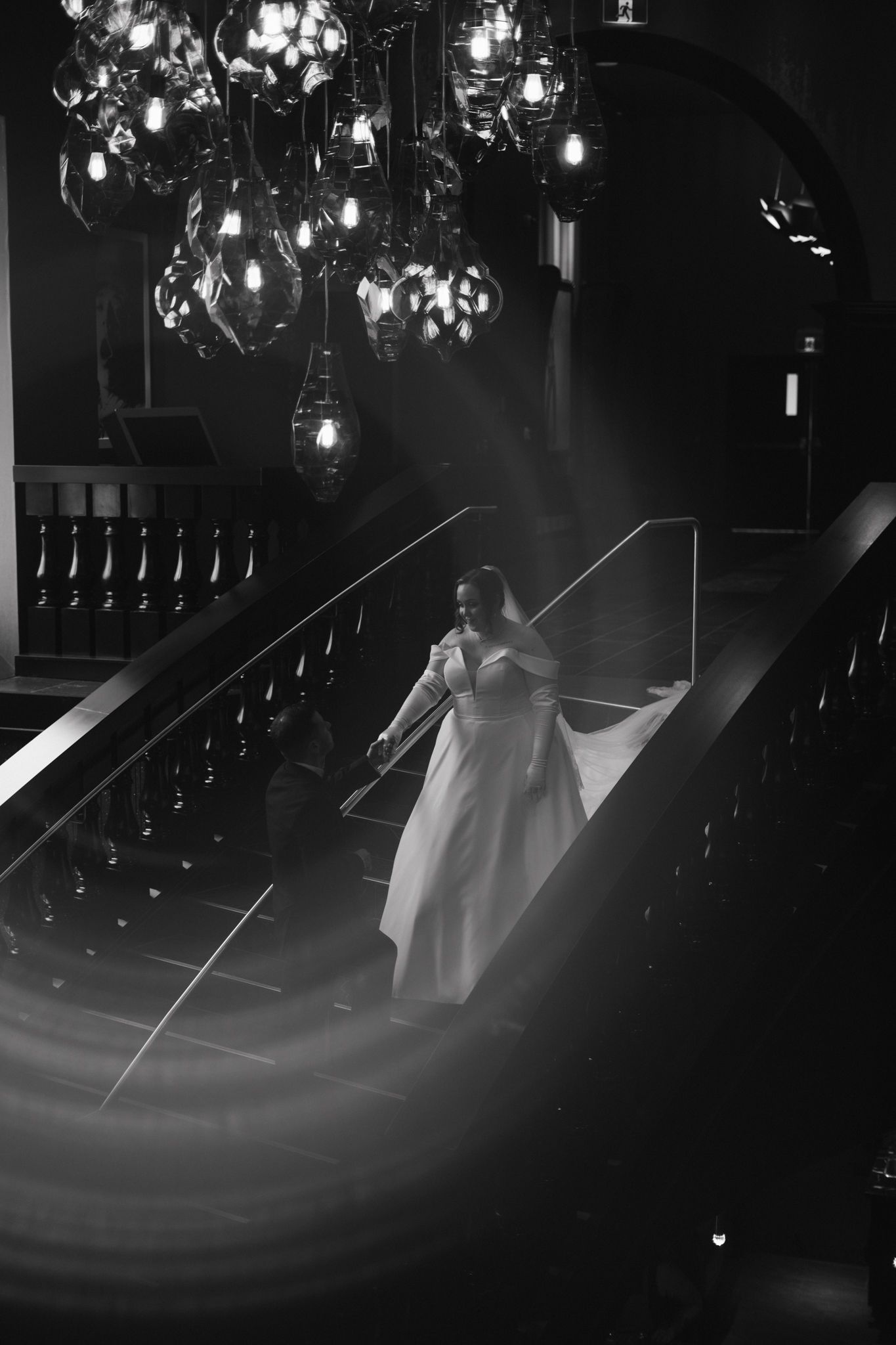 A dreamy silhouette of a wedding dress under hanging lights in a dark venue.