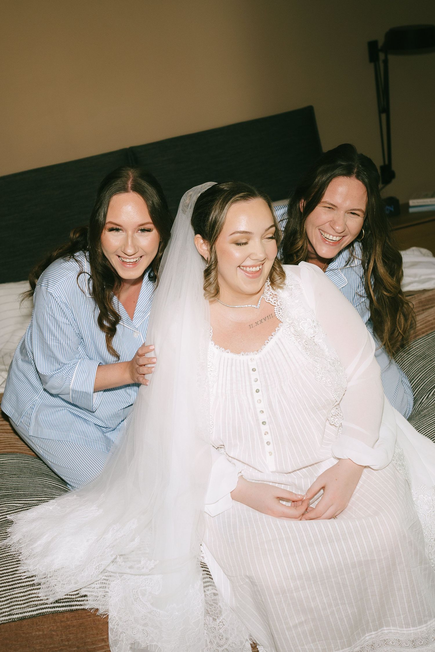 Friends sharing joyful moments while relaxing on a bed in white clothing.