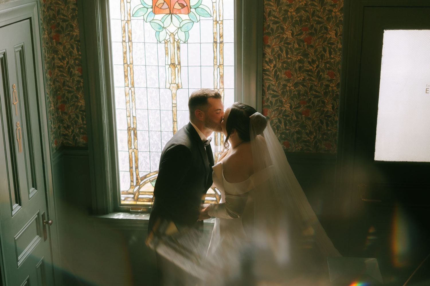 Moody wedding portraits captured against stained glass windows and patterned wallpaper.