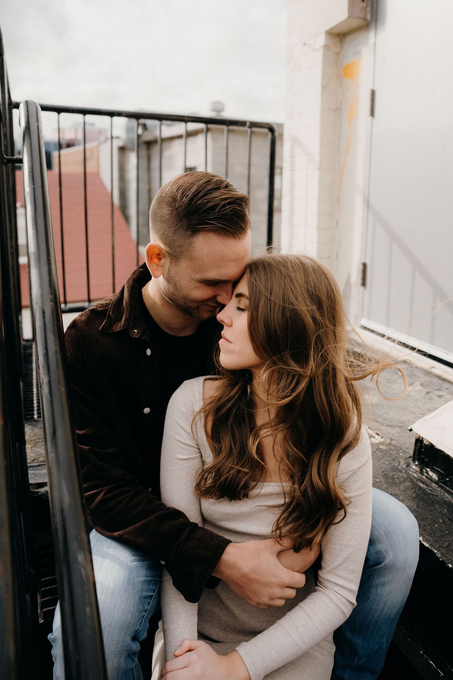 Couple in casual clothing sharing tender moments on an outdoor balcony.