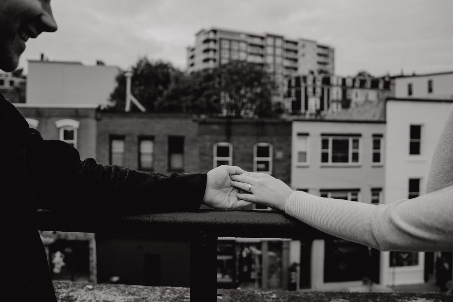 Black and white photo of hands reaching toward each other with city architecture behind.