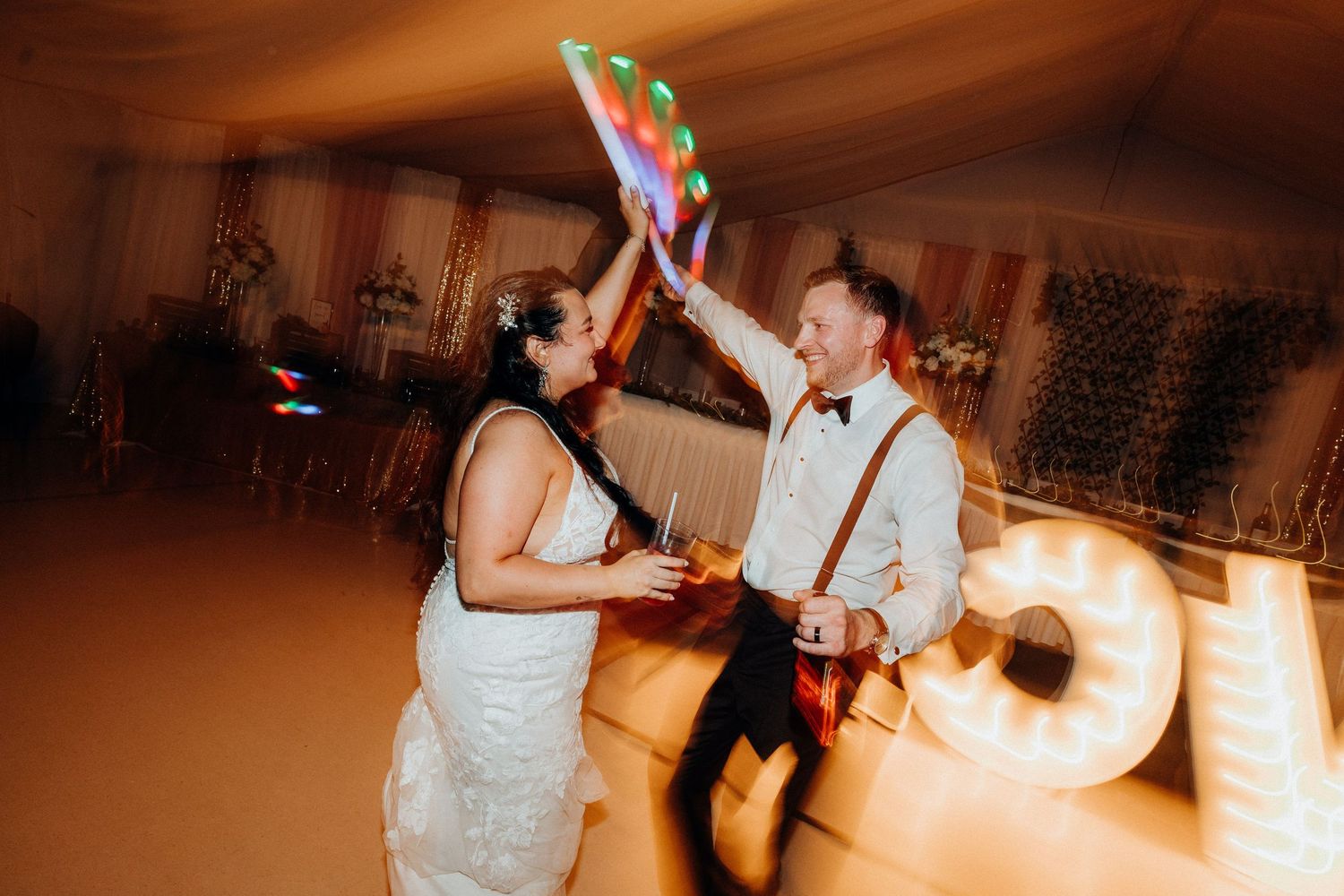 Wedding reception dance floor filled with colorful lights and celebrating guests.