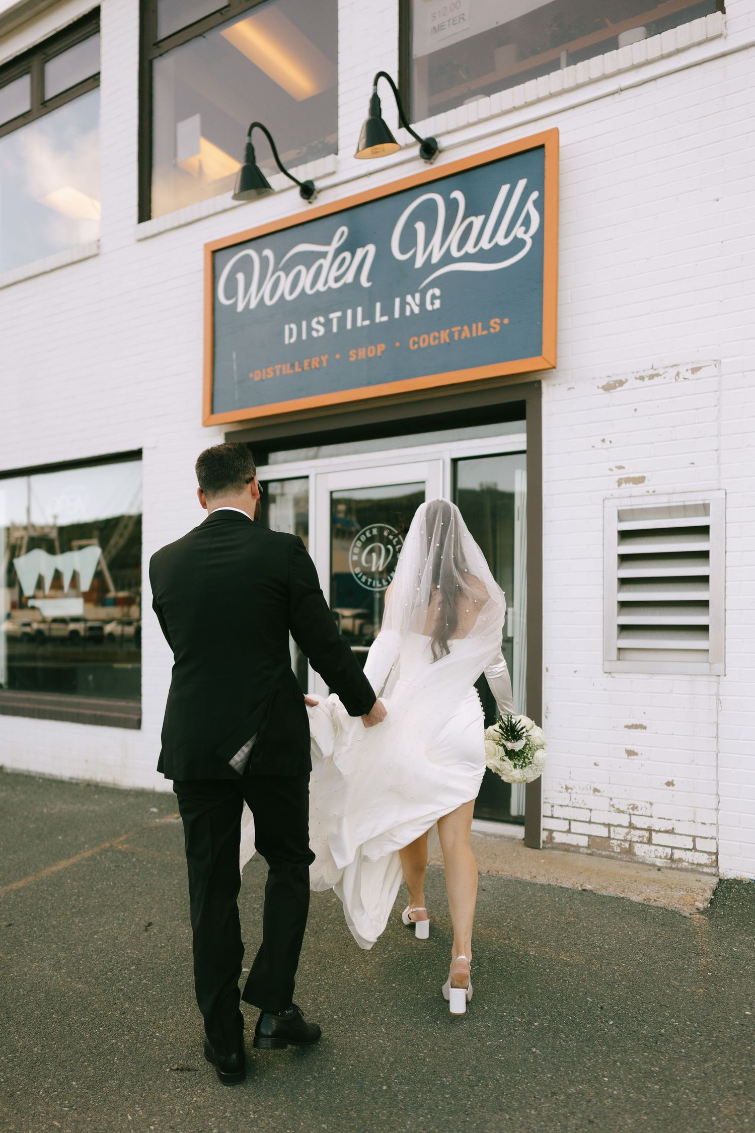 Bride and groom holding hands walking into Wooden Walls Distilling venue on their wedding day.