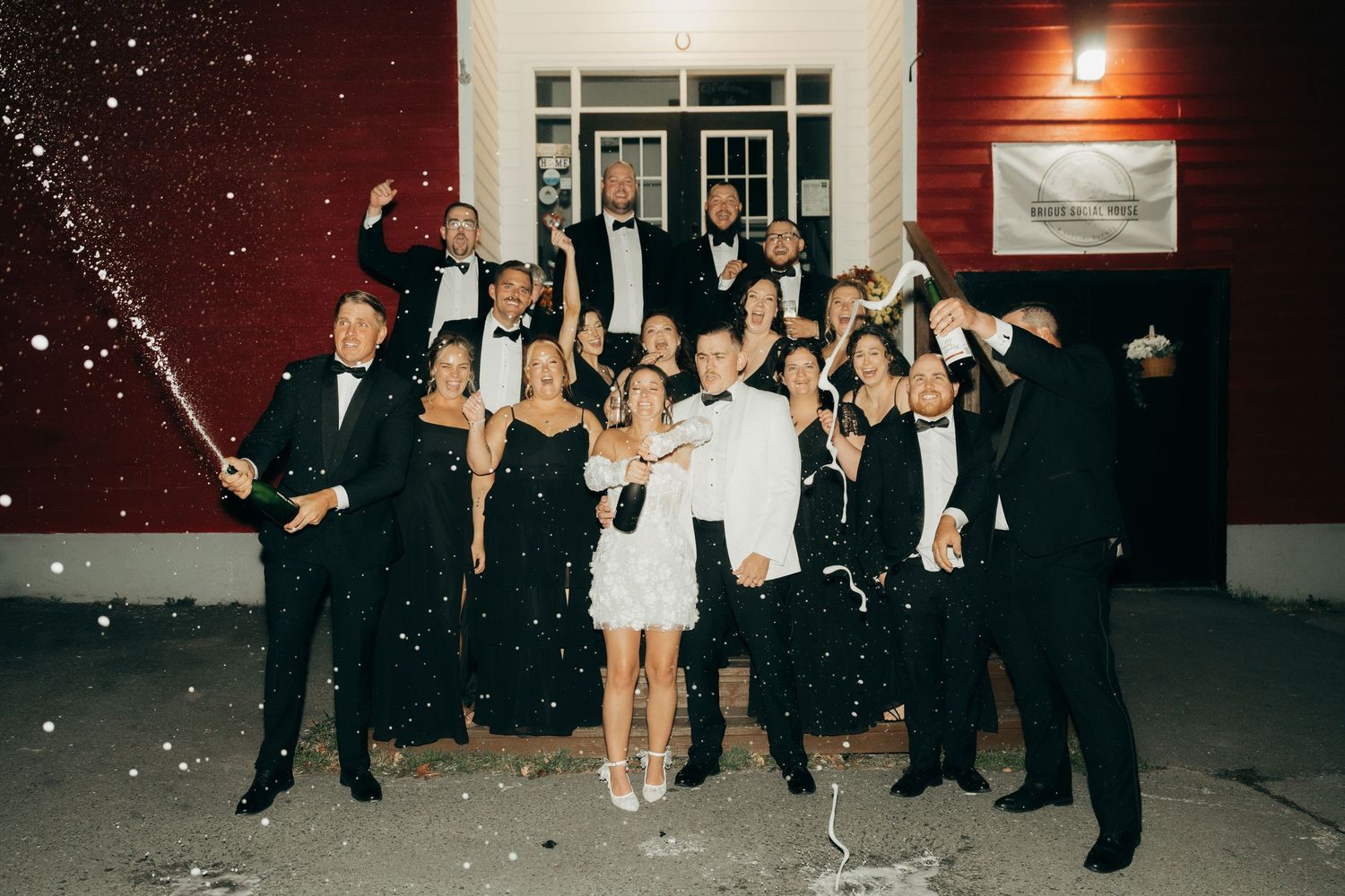 Wedding party celebrates with sparklers at night outside a red-walled venue during a festive reception.
