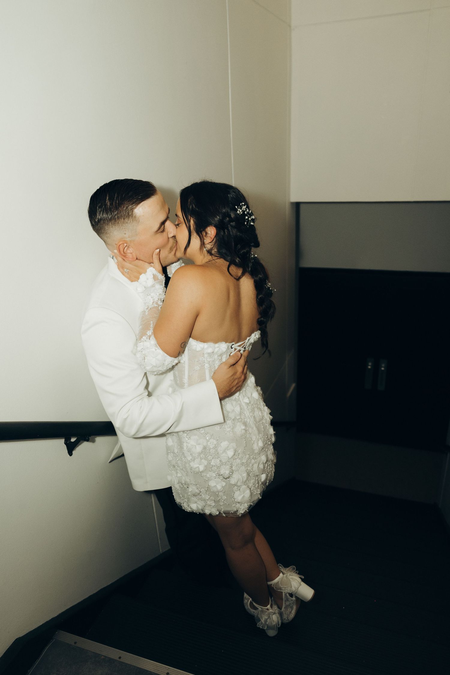 A couple shares an intimate moment in formal attire, with the bride wearing a short white dress and lace shoes.