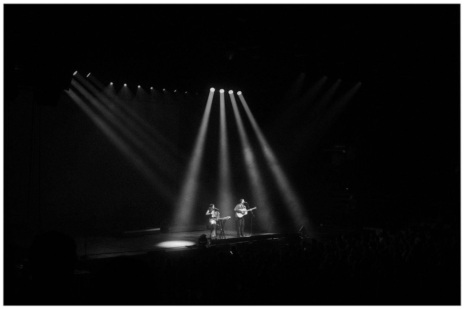 Dramatic spotlights illuminate a dark stage with beams of light creating atmospheric rays in a performance space.