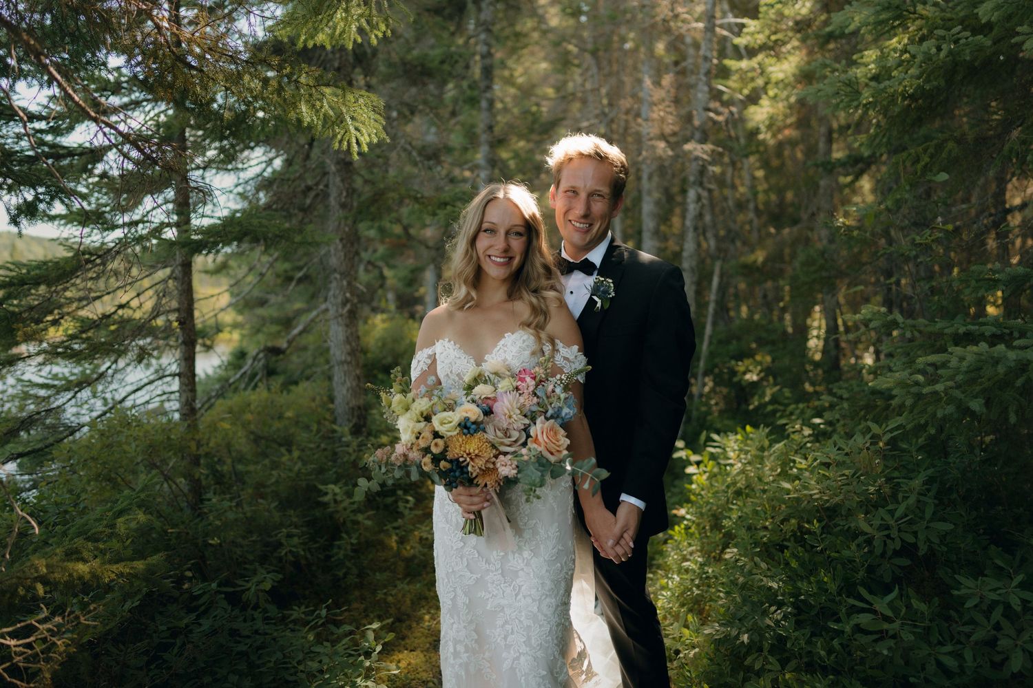 A couple poses together in a lush forest setting with sunlight filtering through the trees during their wedding photoshoot.