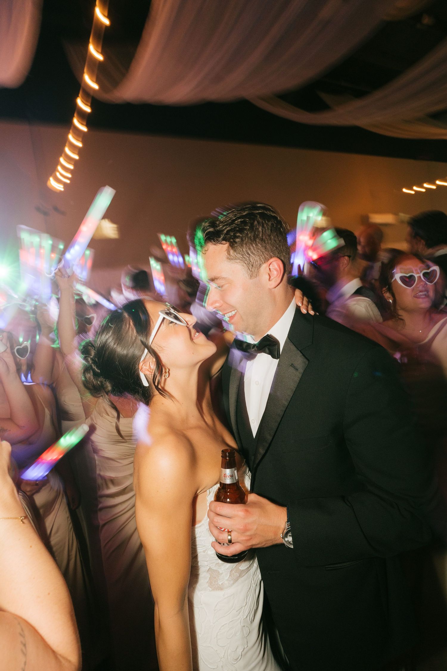 Bride and groom share a romantic moment on the dance floor surrounded by guests with glowing light sticks at their wedding reception.