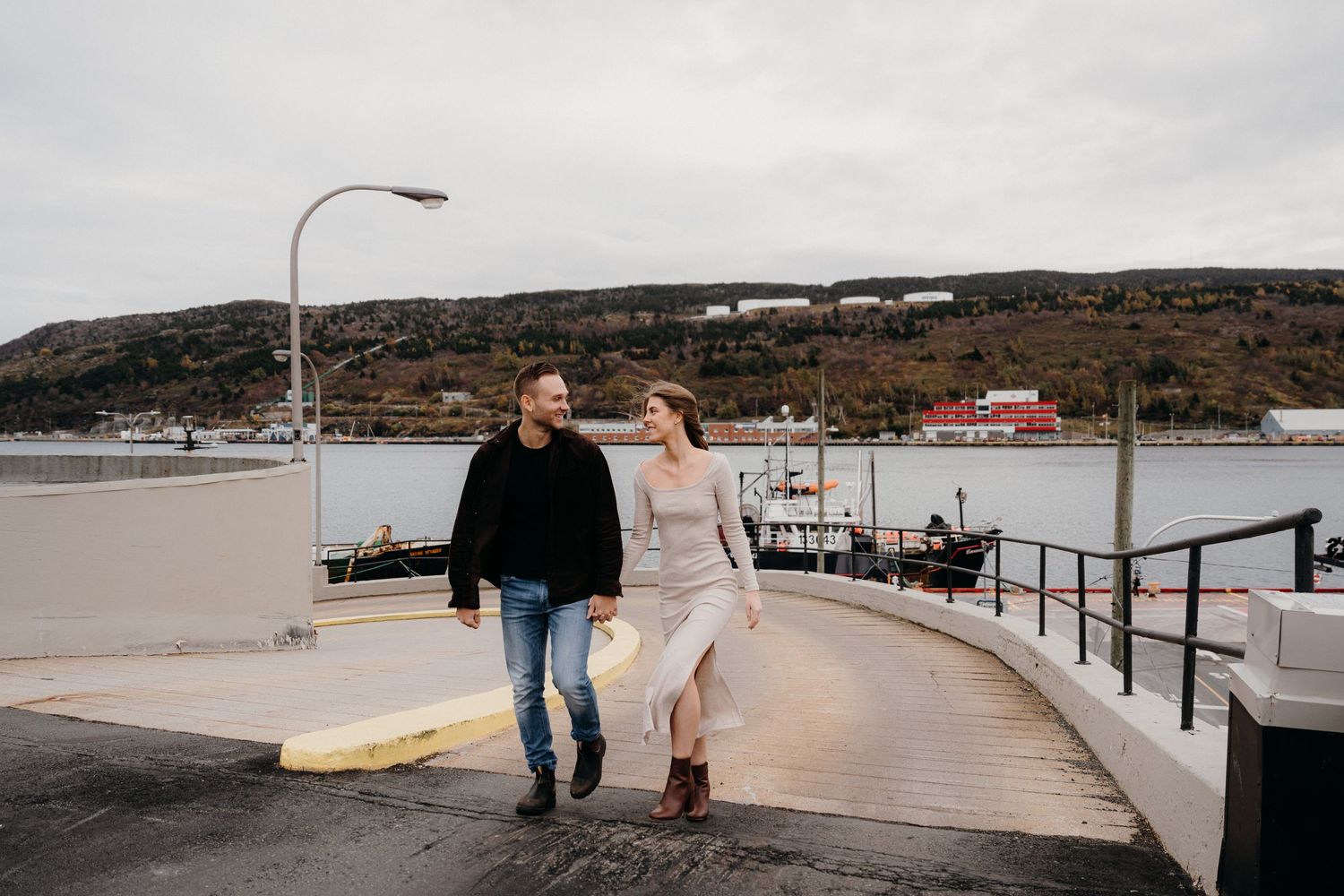 People strolling on a coastal walkway with harbor views and cloudy skies overhead.