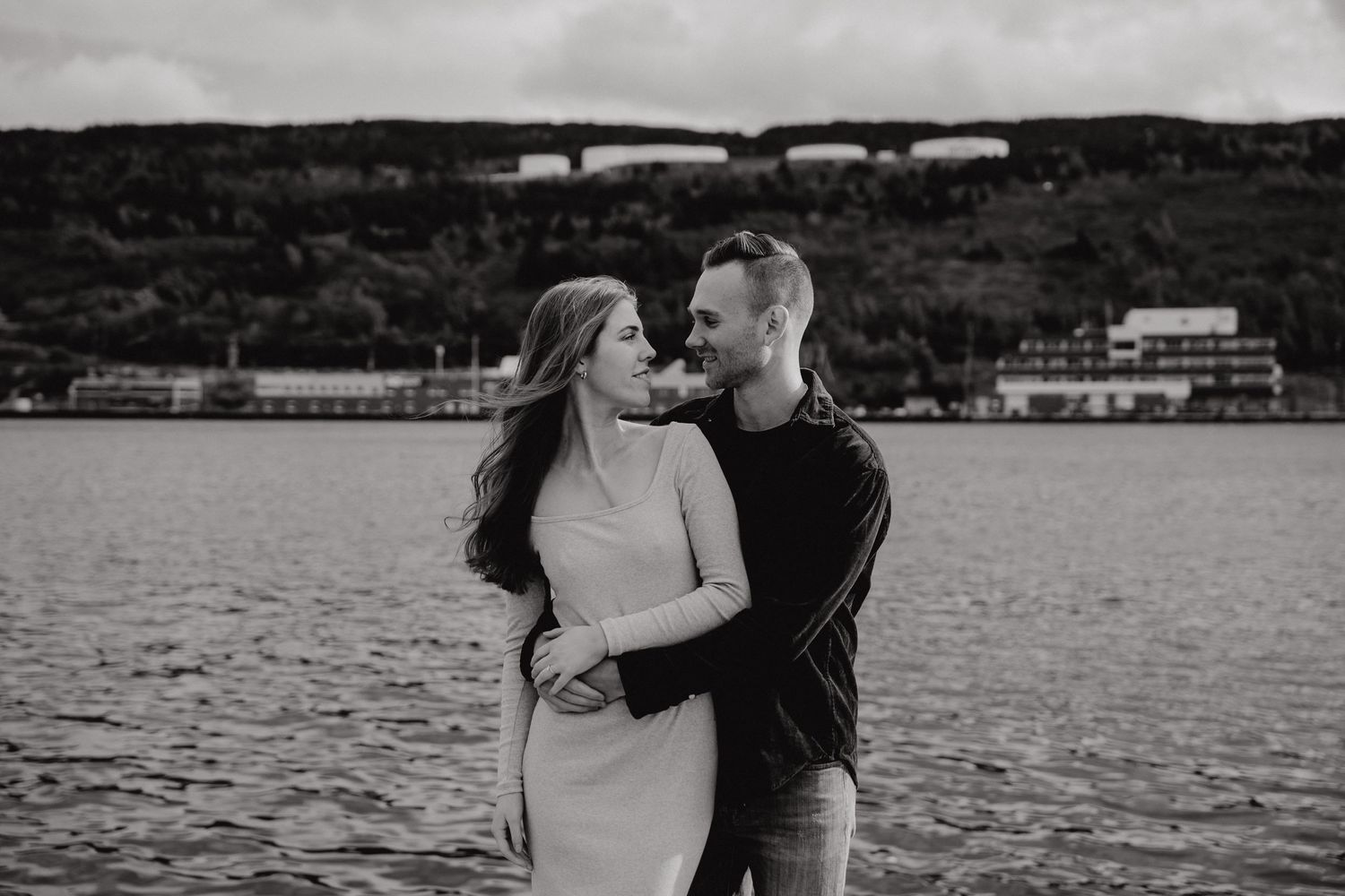 A couple's portrait session along the harbor with mountains and industrial buildings in the distance.