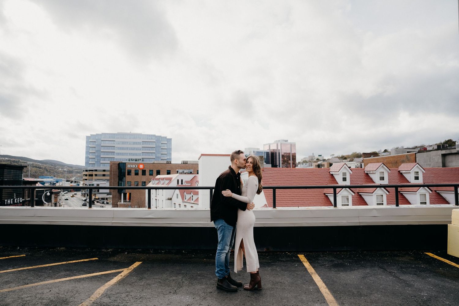 A tender moment between two people on a parking structure overlooking the city skyline.