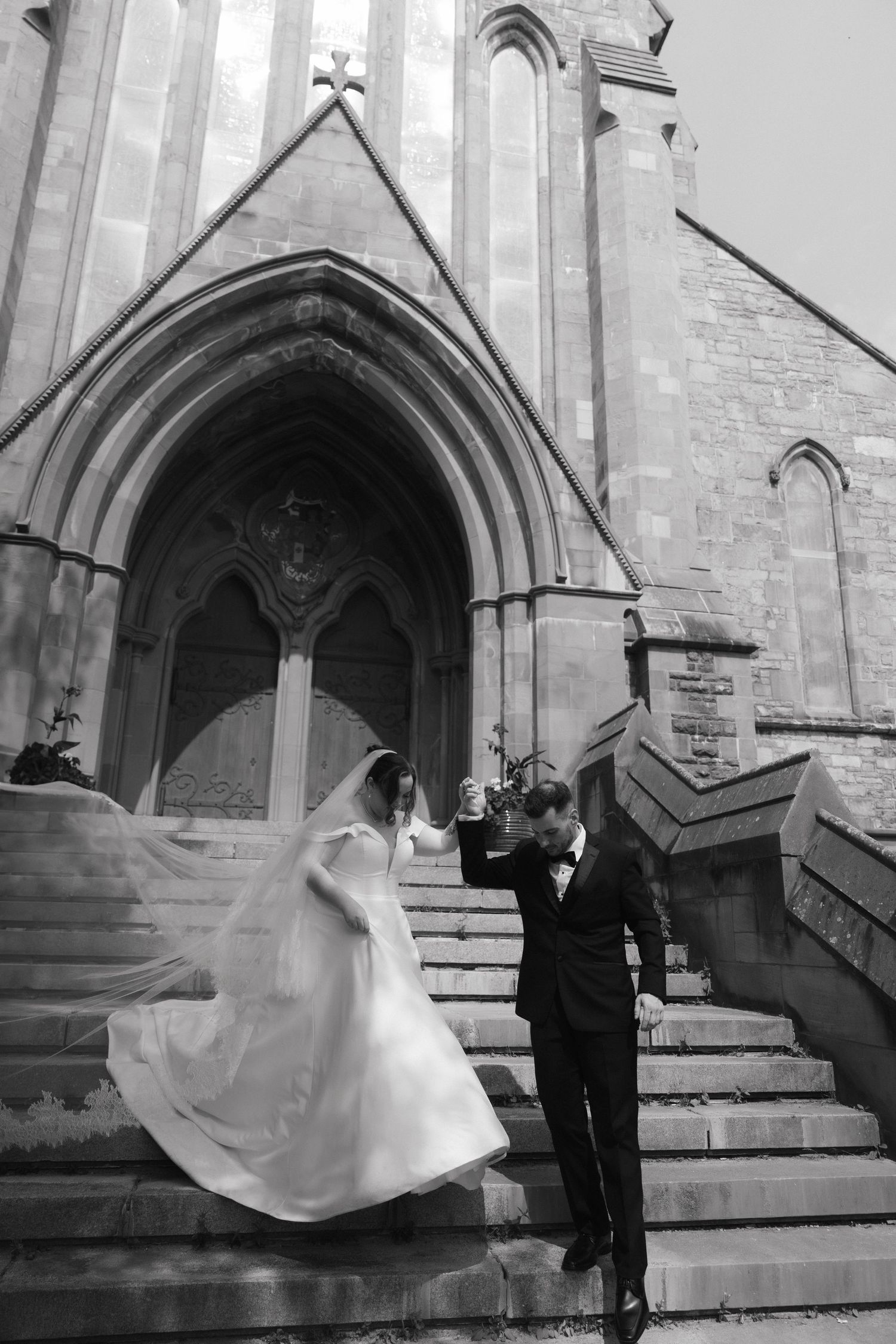 Black and white wedding photos with dramatic veil movement outside a stone church entrance.