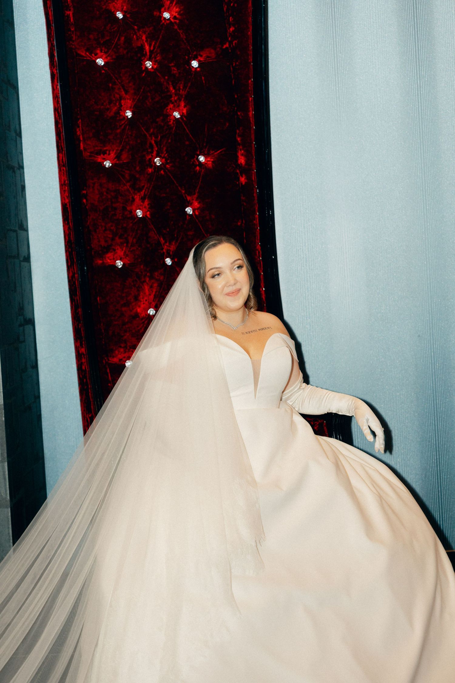 Artistic bridal portraits with flowing white gown against red velvet and blue wall backdrop.