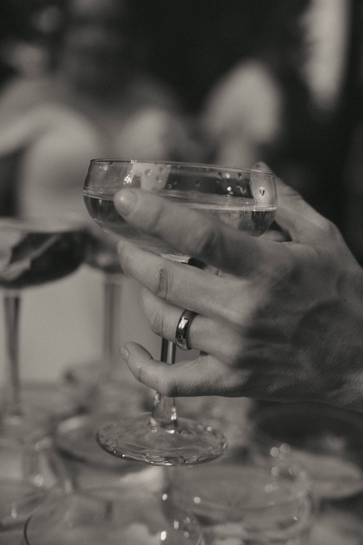 Black and white close-up of a hand holding a champagne glass with a wedding ring.