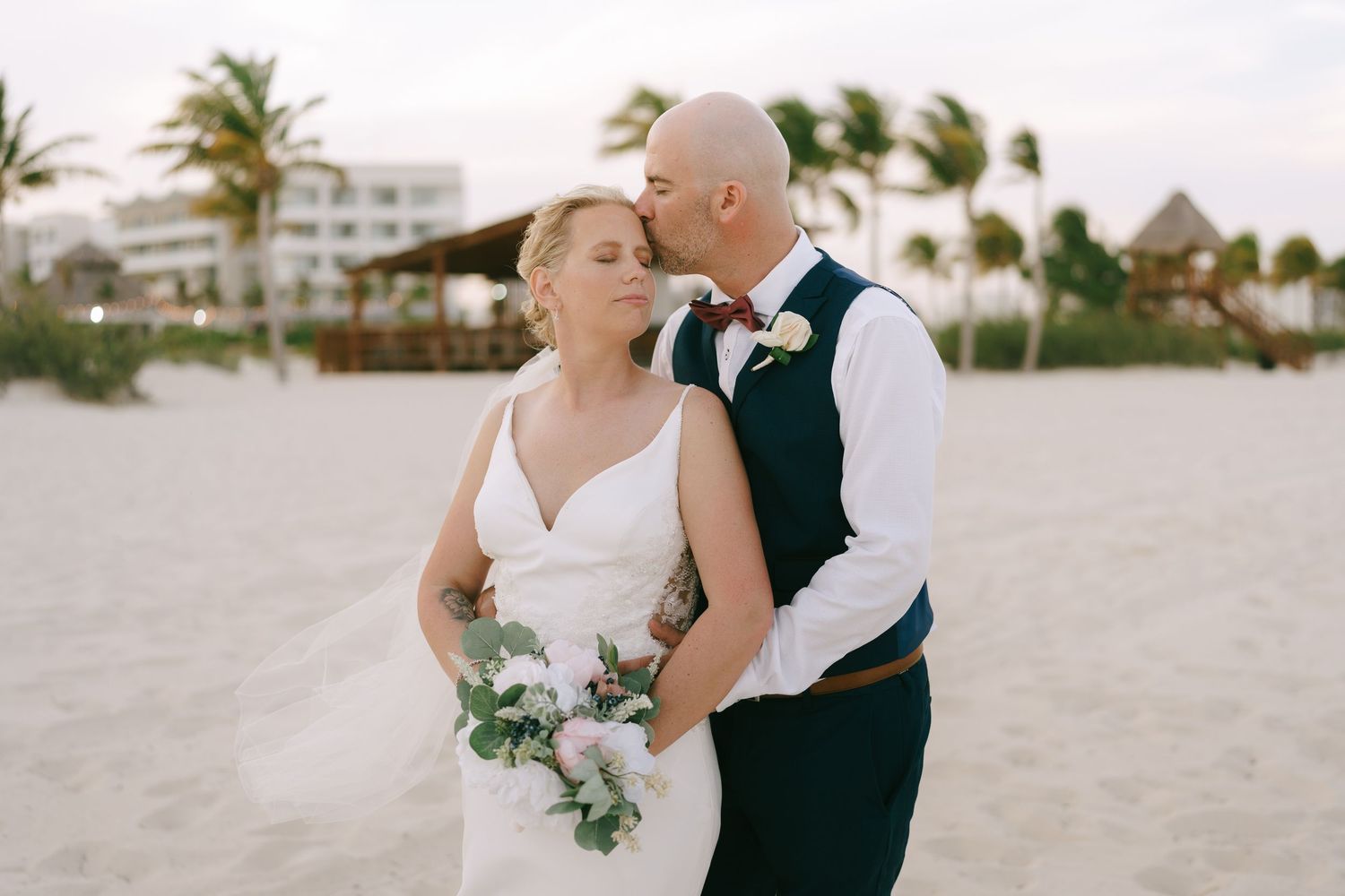 Romantic beach wedding portrait with palm trees and ocean backdrop.