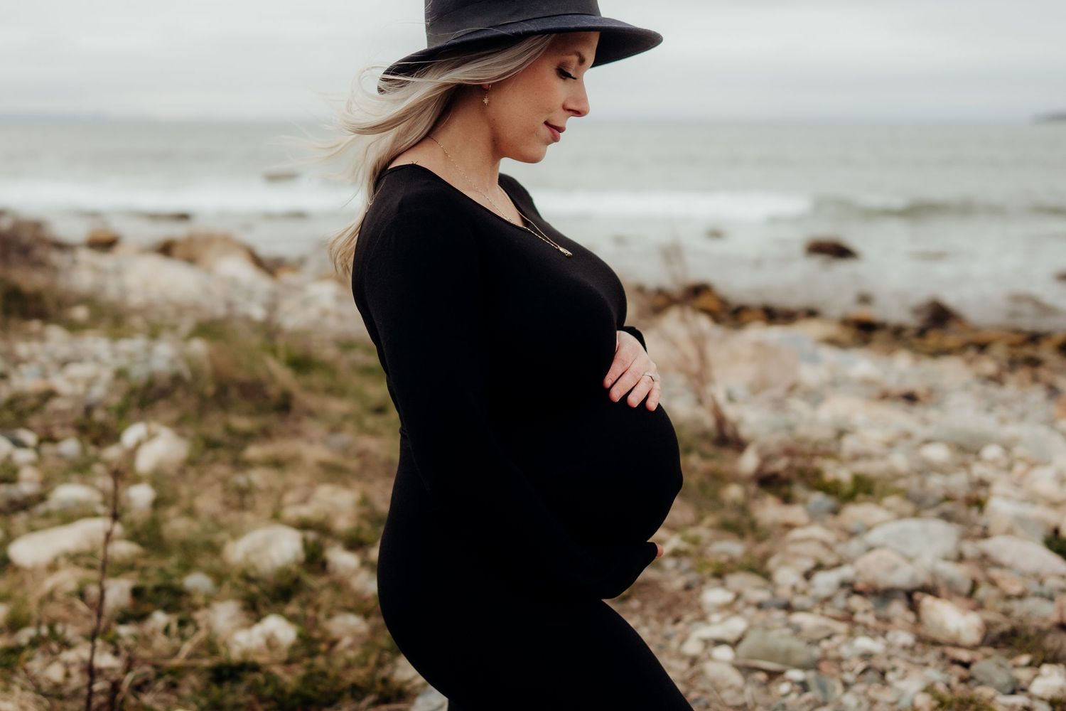 Maternity photos captured on rocky beach shoreline under moody skies.