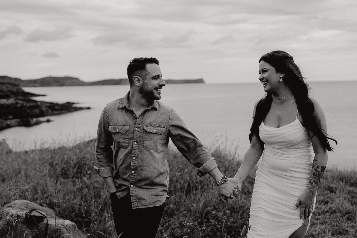 A couple embraces while standing along a scenic rocky coastline during an overcast day.