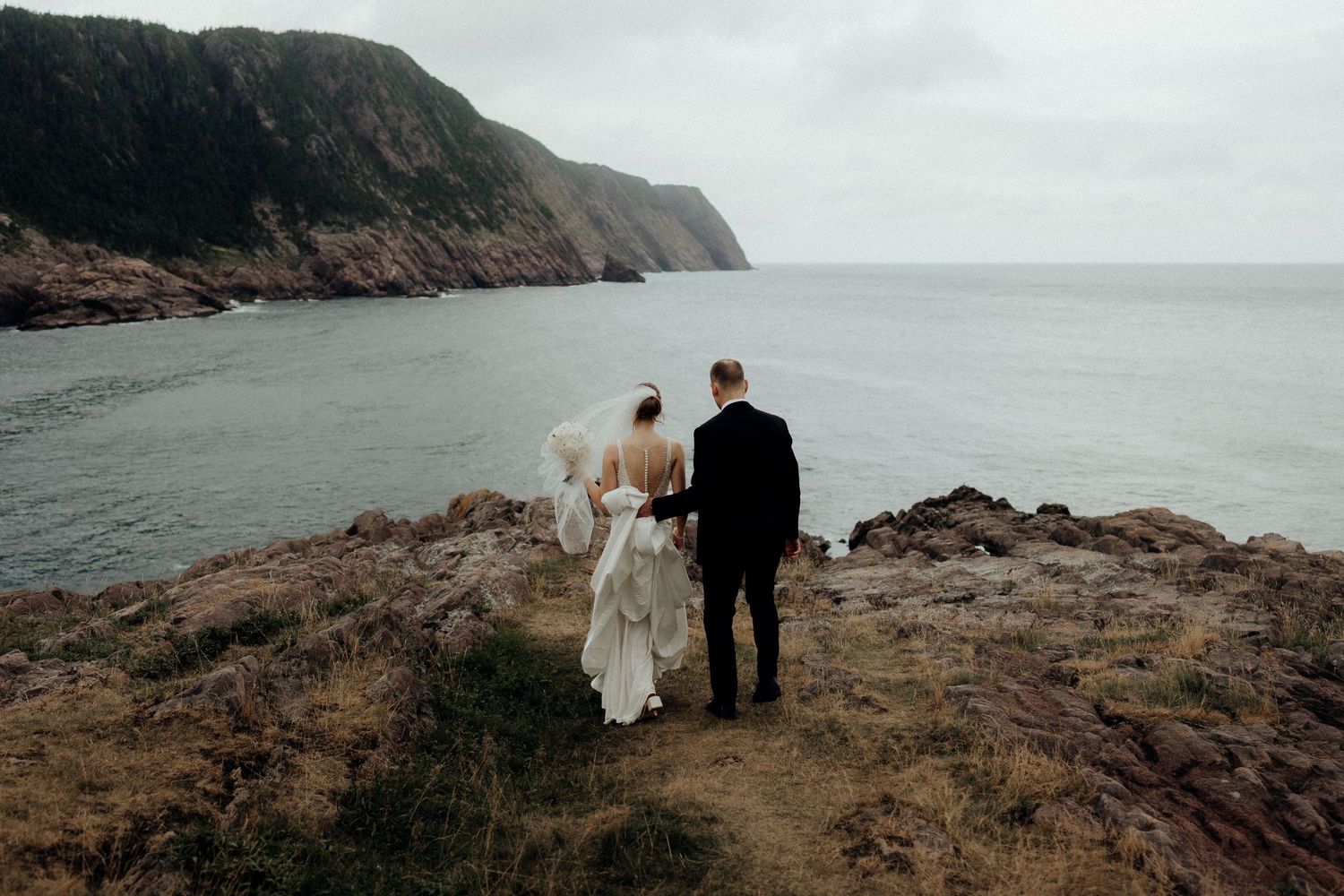 Couple standing at cliff edge overlooking dramatic coastal landscape.