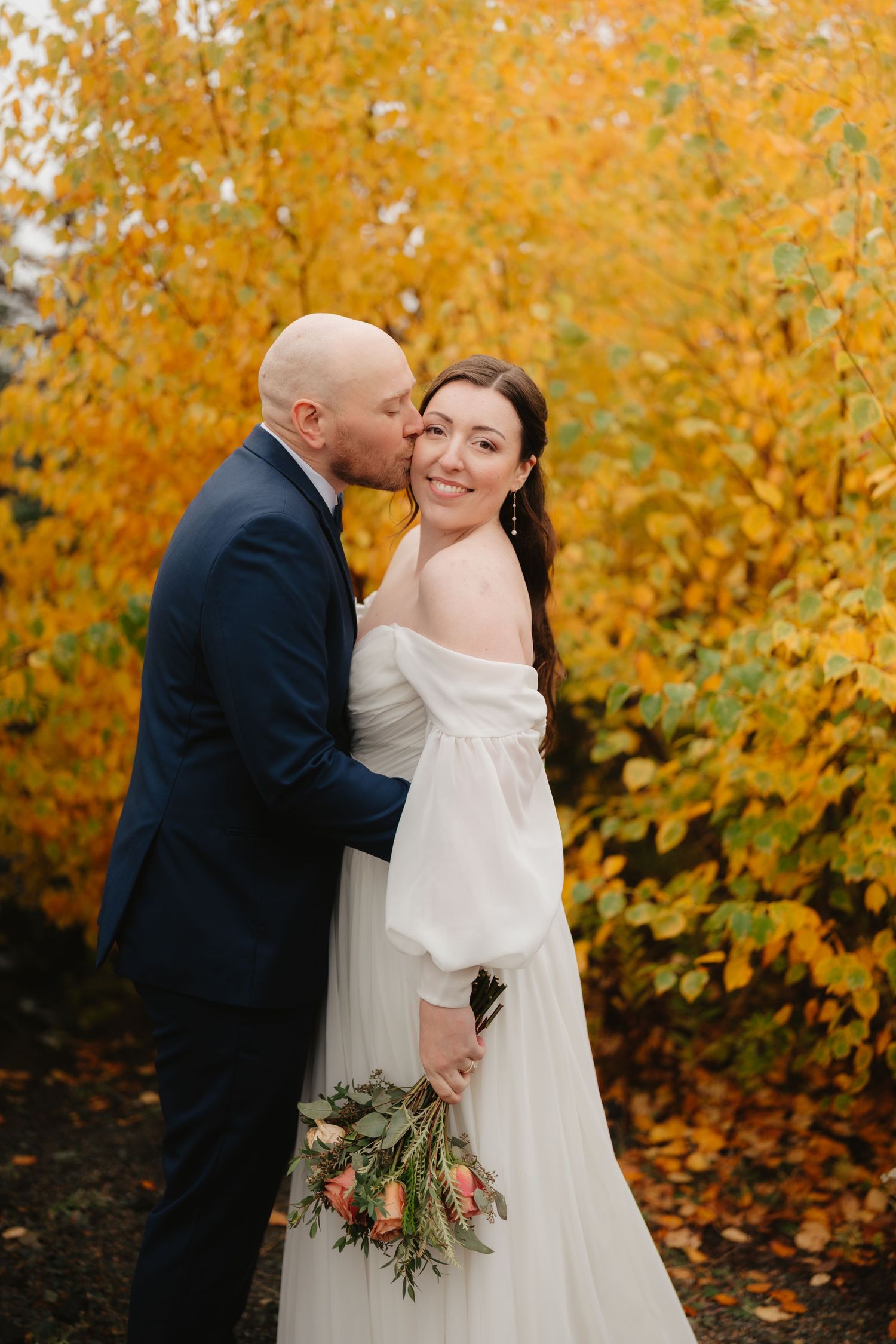 A couple shares an intimate moment against a backdrop of vibrant autumn foliage during their wedding photoshoot.
