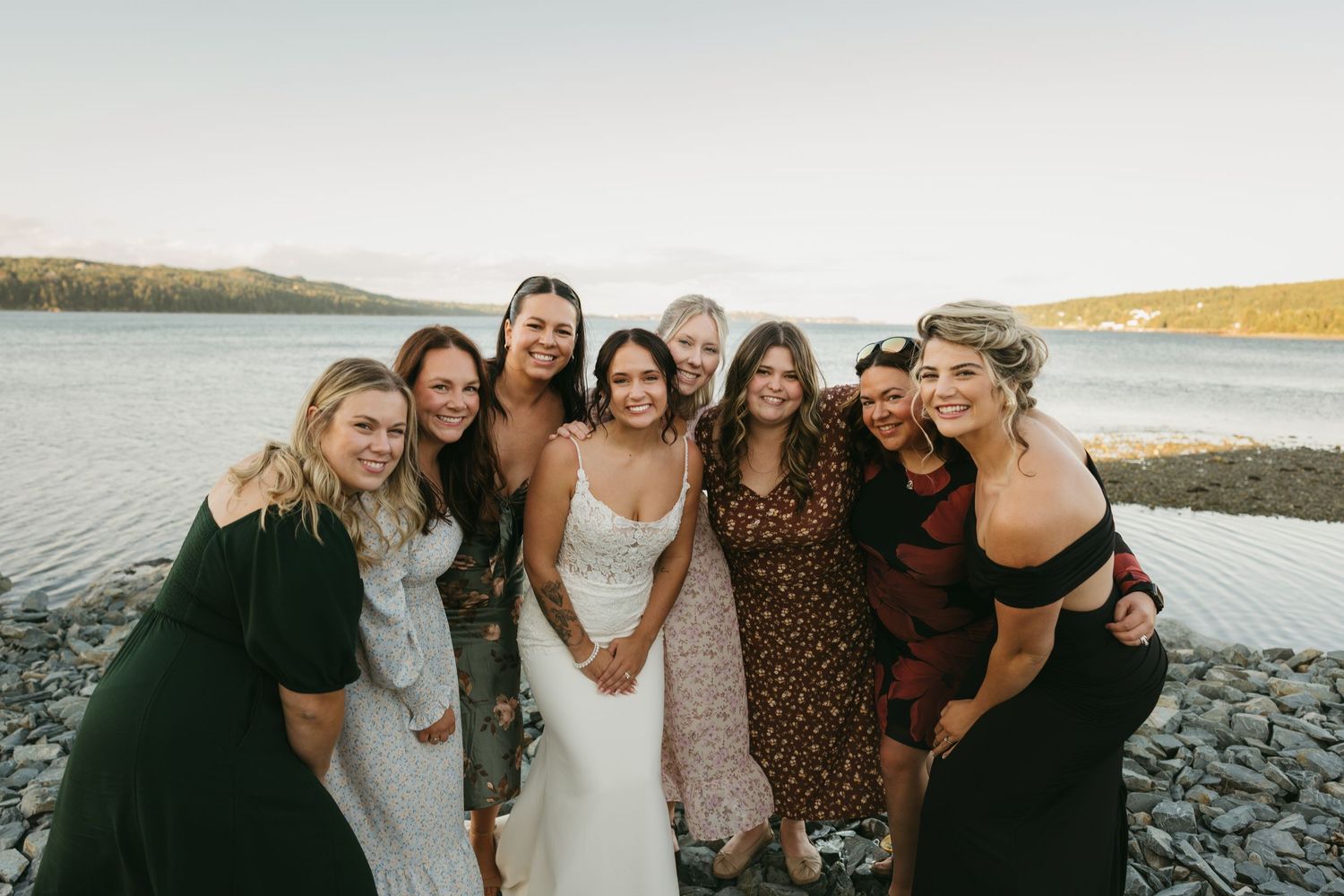 A group of friends laugh together while standing on a rocky beach at sunset.