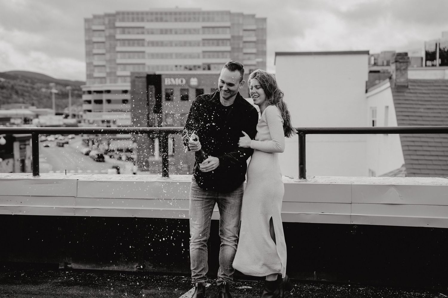 A couple shares a romantic moment on an urban rooftop with city buildings in the background.
