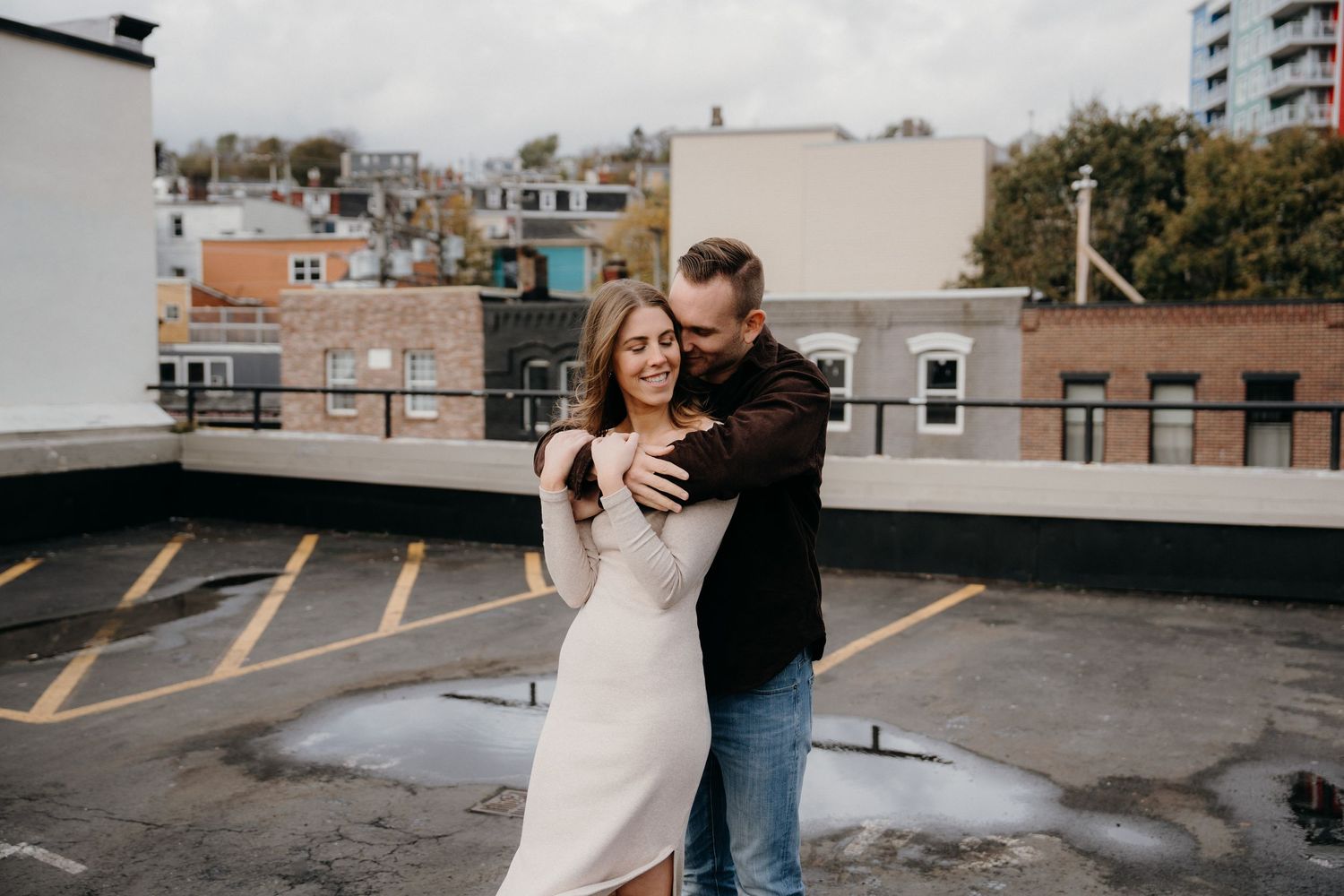 Couple in casual attire shares romantic embrace on urban rooftop with parking lines.