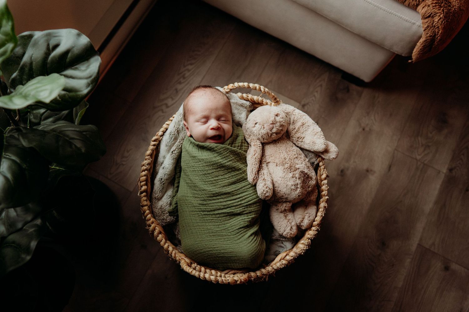Side angle view of baby sleeping in basket with plush toy and green wrap.