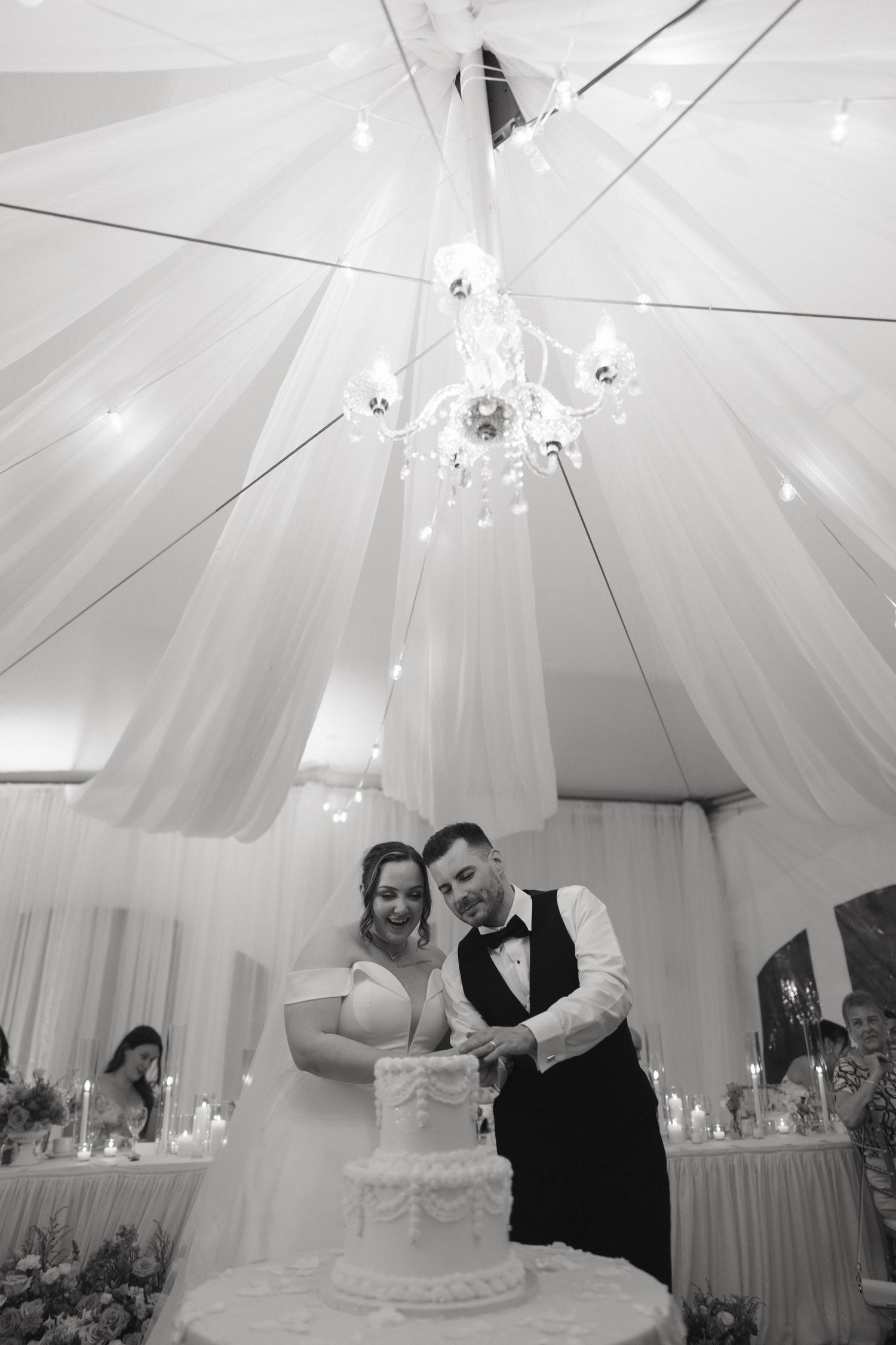 Monochrome wedding reception scene under a beautifully draped white tent ceiling.