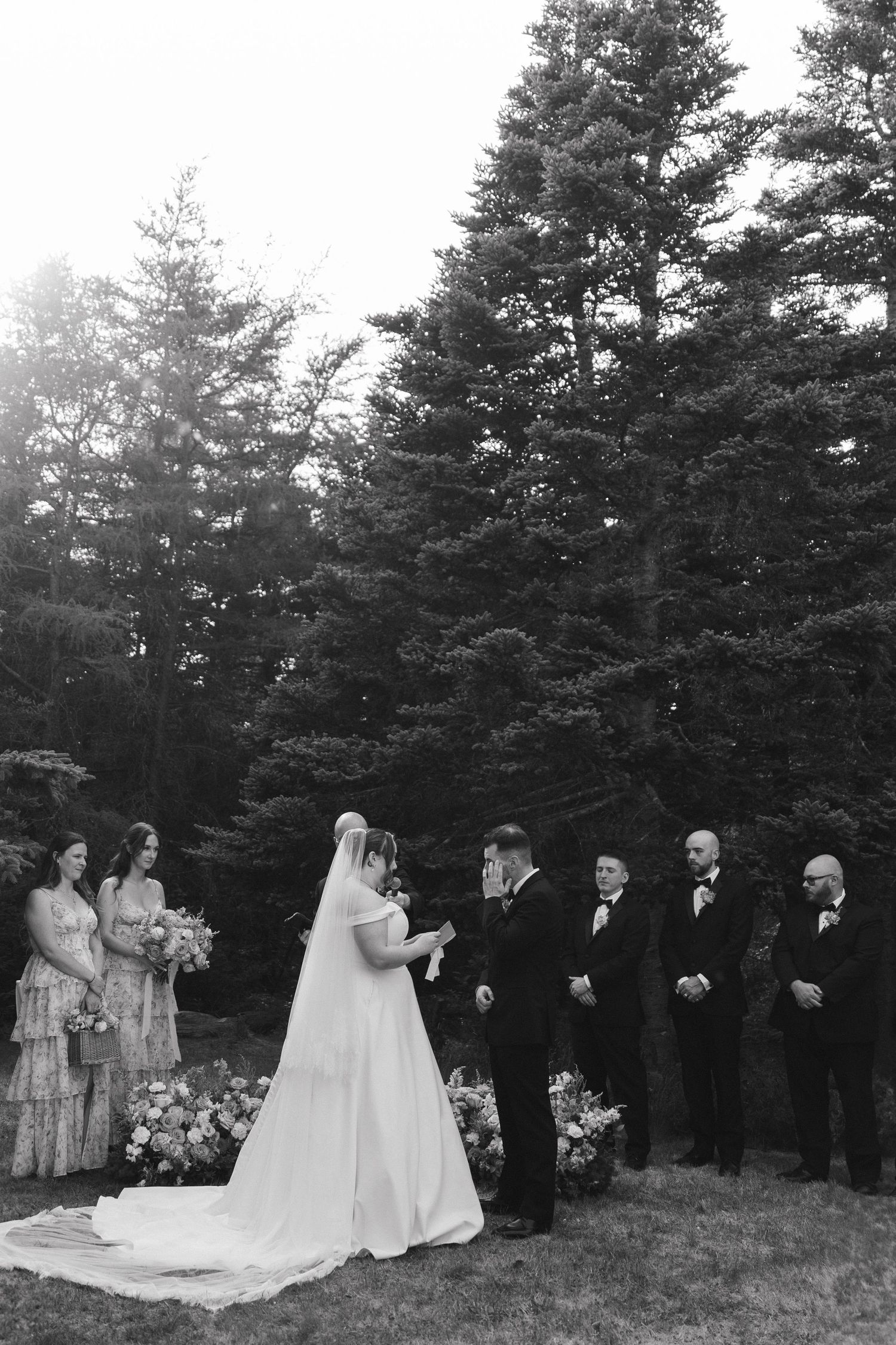 Wedding party lined up against evergreen forest backdrop during outdoor ceremony.