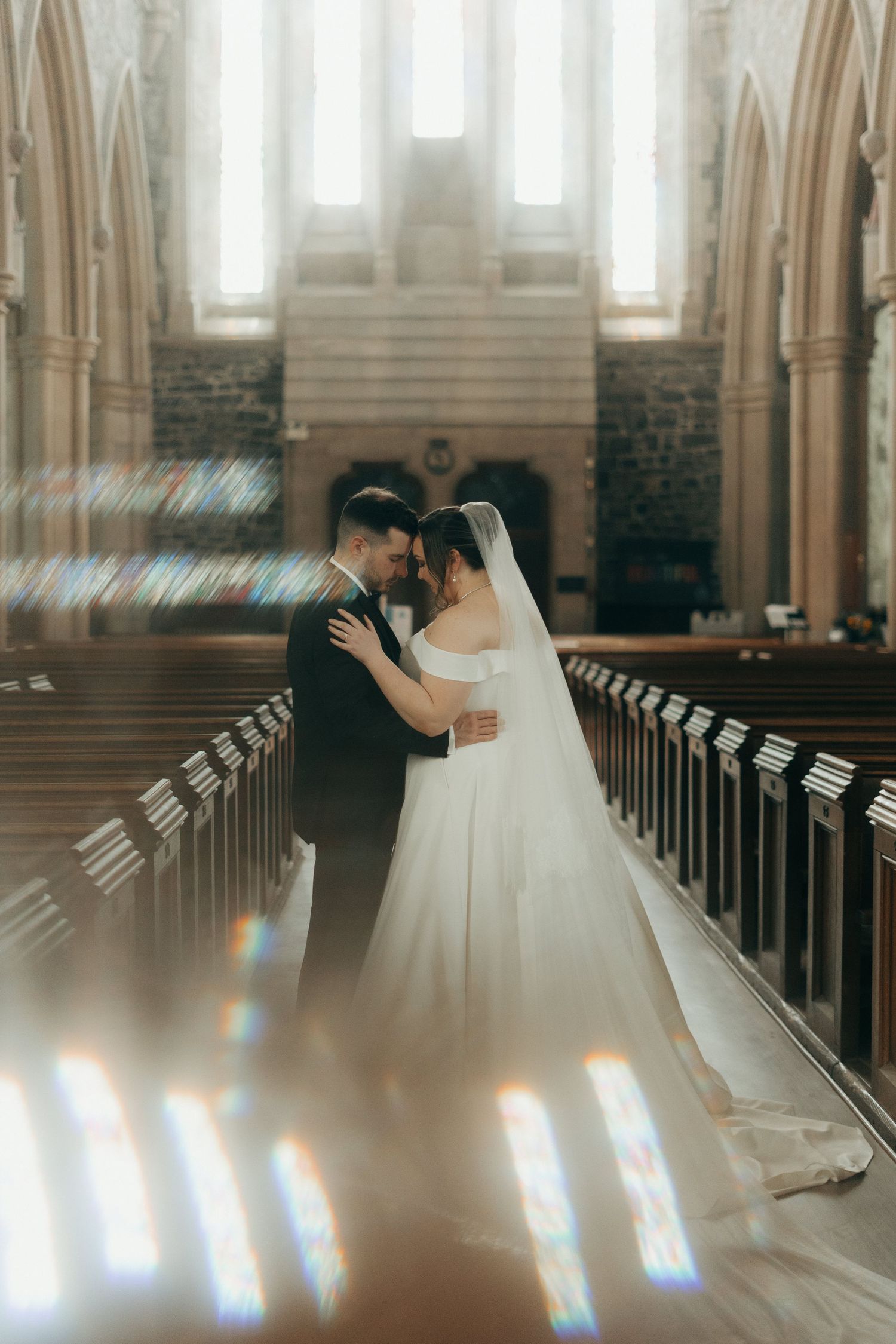 Romantic church wedding moment captured in soft, ethereal light streaming through windows.