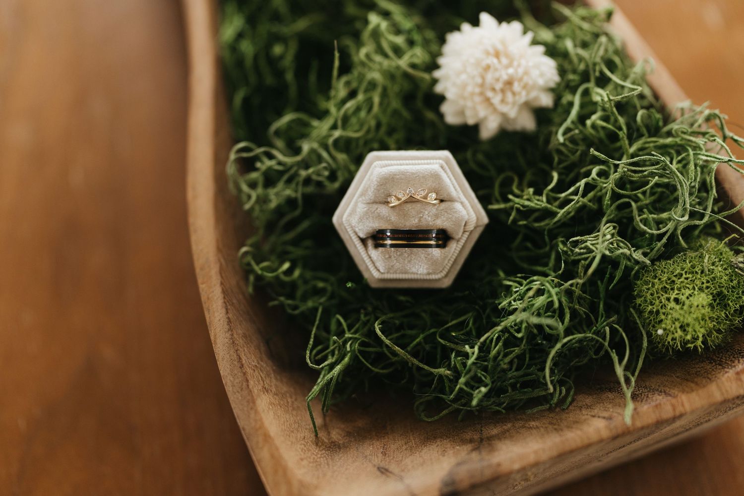 Decorative arrangement featuring white flowers and green moss in a rustic wooden container.