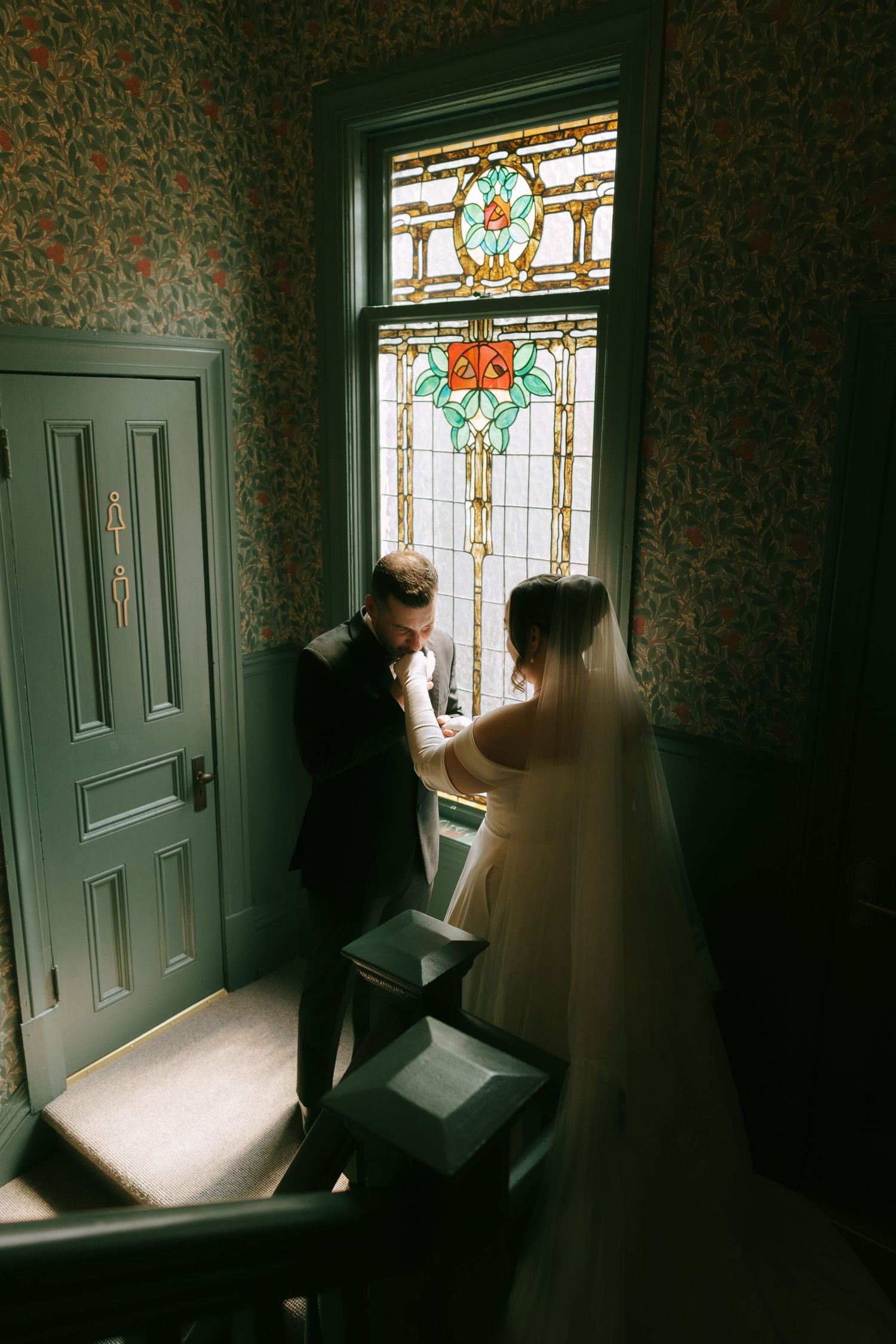 Silhouetted figures near ornate stained glass window in vintage setting.