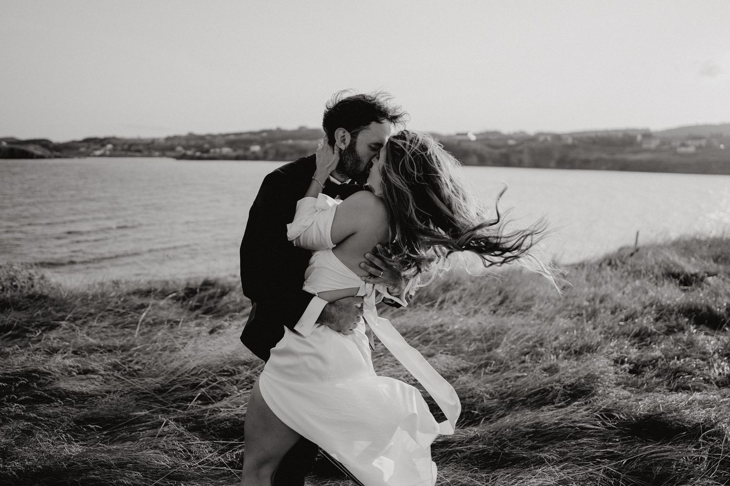 Wedding couple walking through windswept grass along a dramatic coastline.