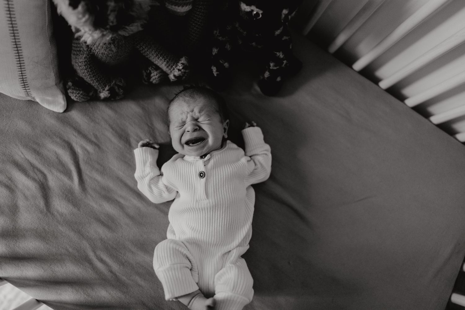 Wide angle shot of baby in white onesie lying in crib.