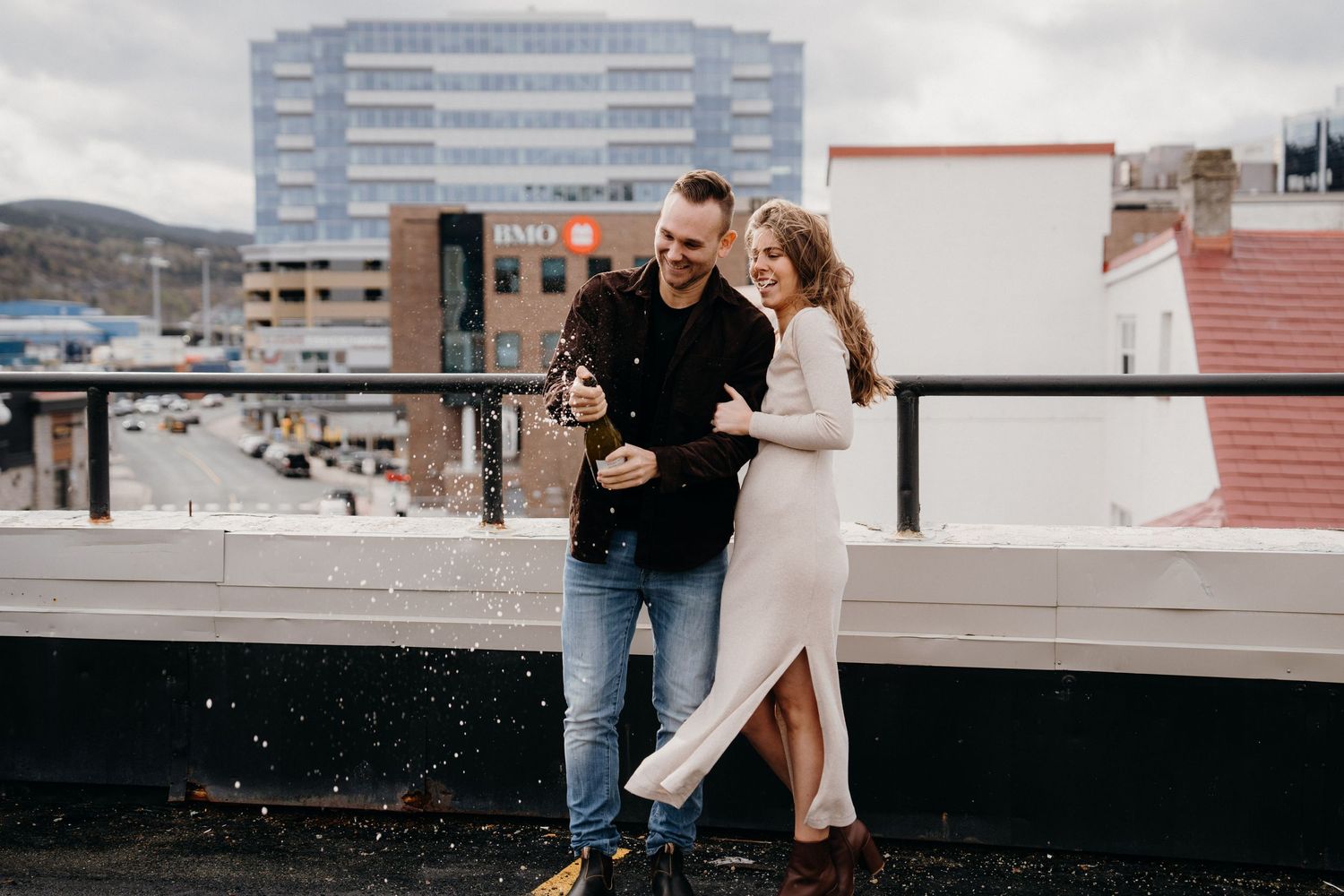 A couple shares a romantic moment on an urban rooftop with city buildings in the background.
