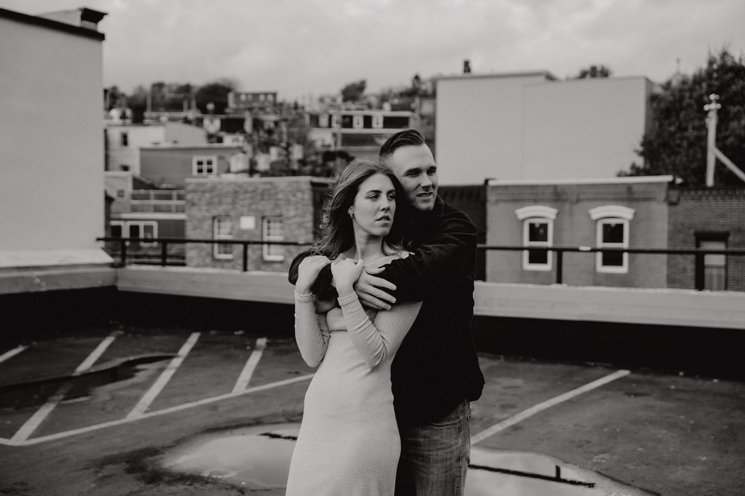Romantic couple embraces on urban rooftop parking lot during black and white photo session.