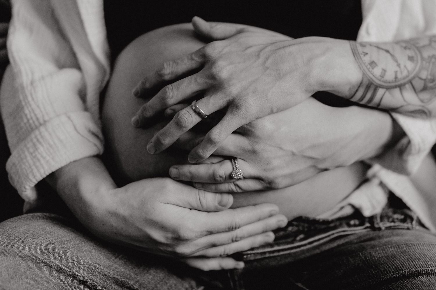 Black and white close-up of hands tenderly resting on a pregnant belly.