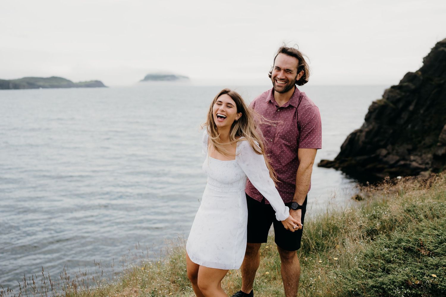 Couple laughs together while enjoying views from a coastal cliff overlook.