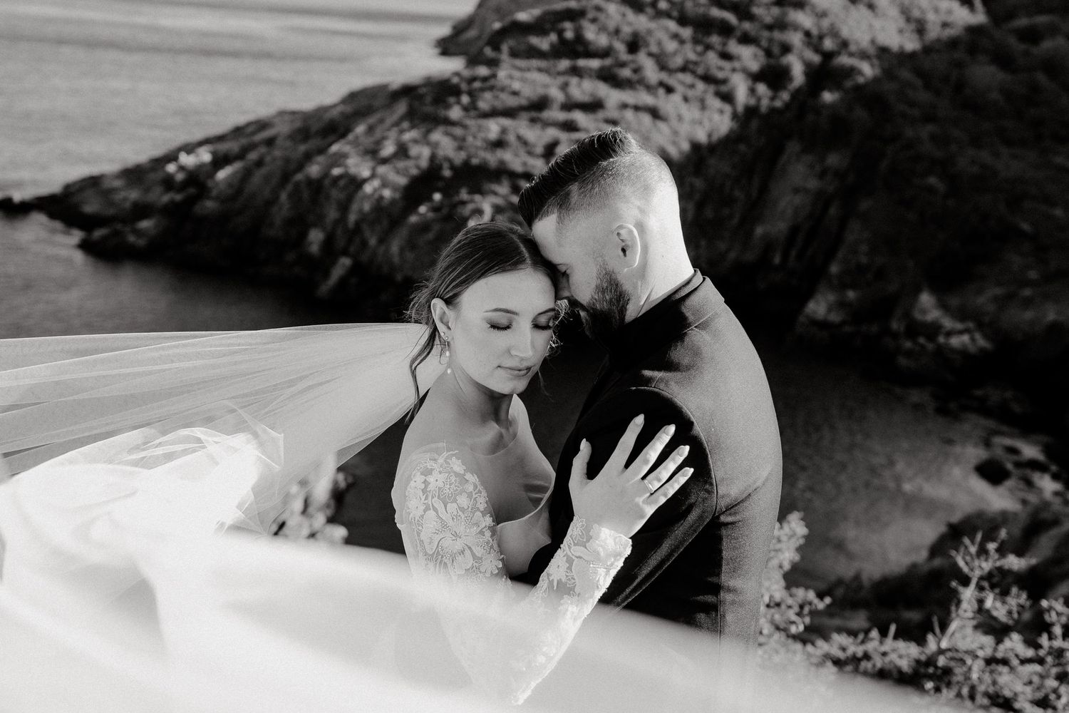 Couple embracing on rocky coastal landscape with dramatic lighting.
