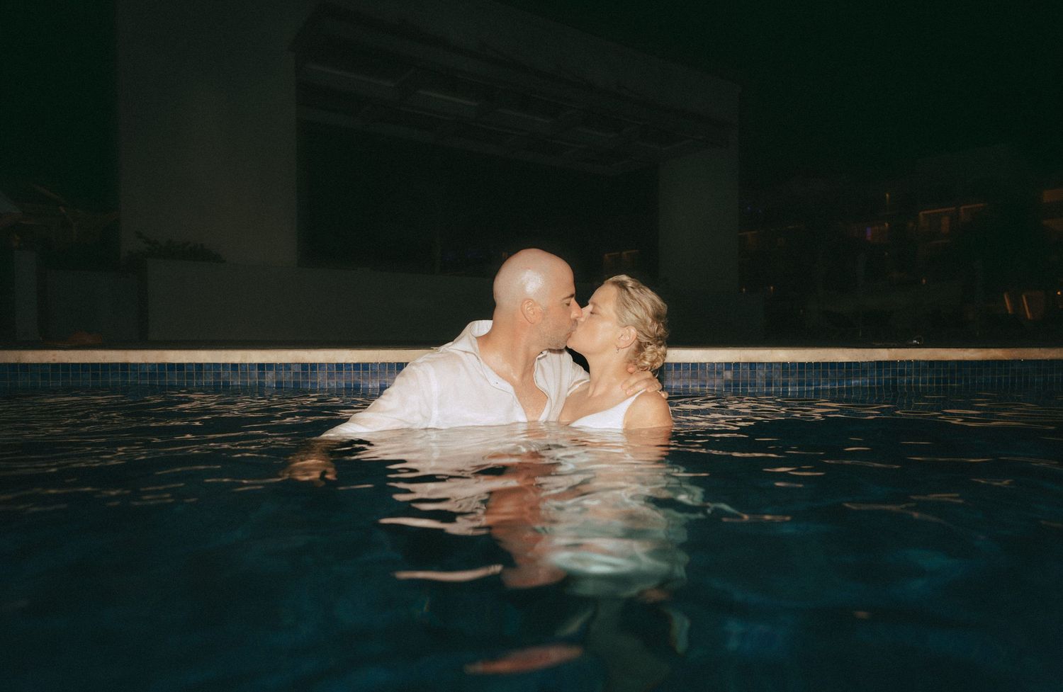 Romantic nighttime pool photoshoot with a couple in wedding attire.