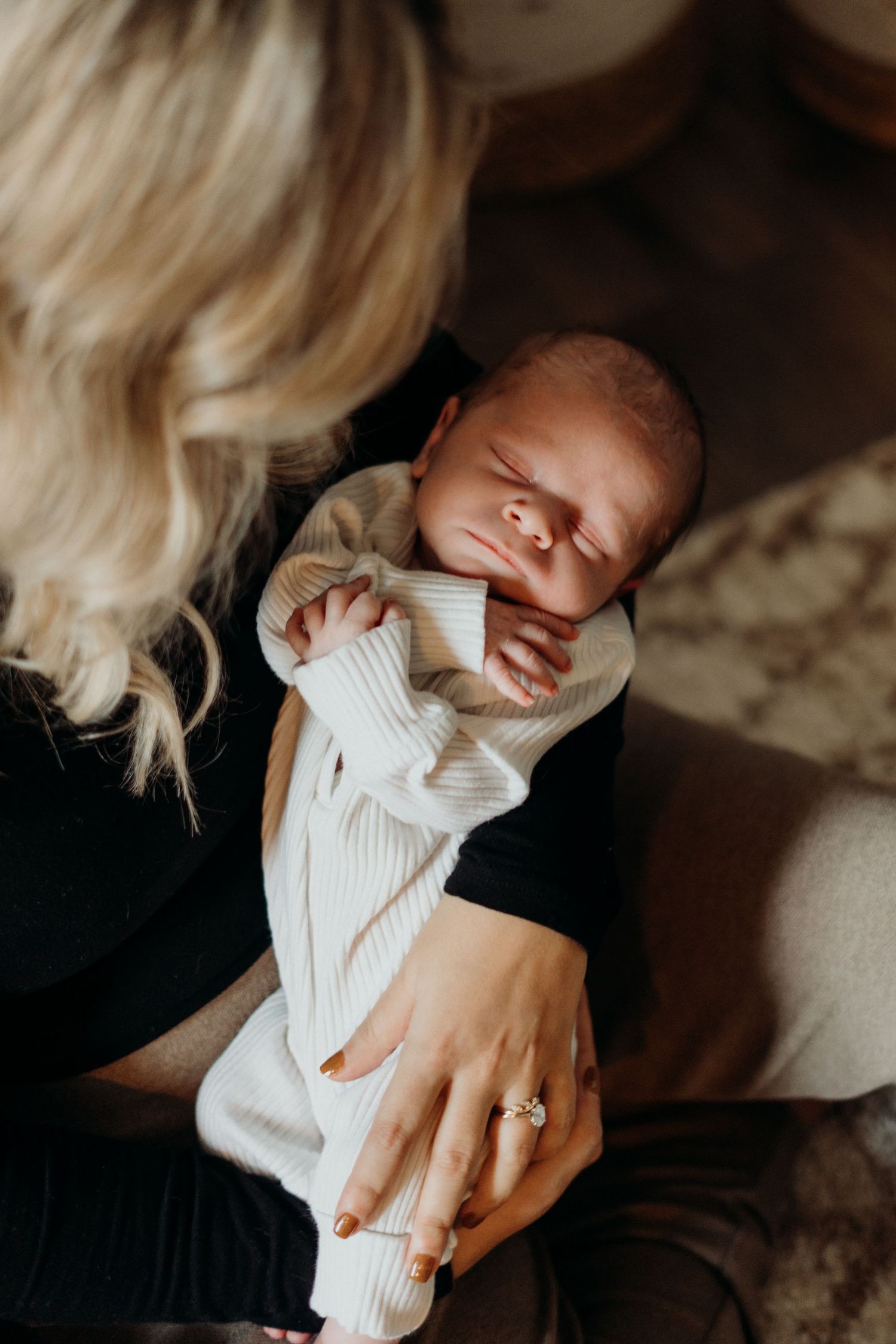Sleeping newborn in white sweater being held against dark clothing.