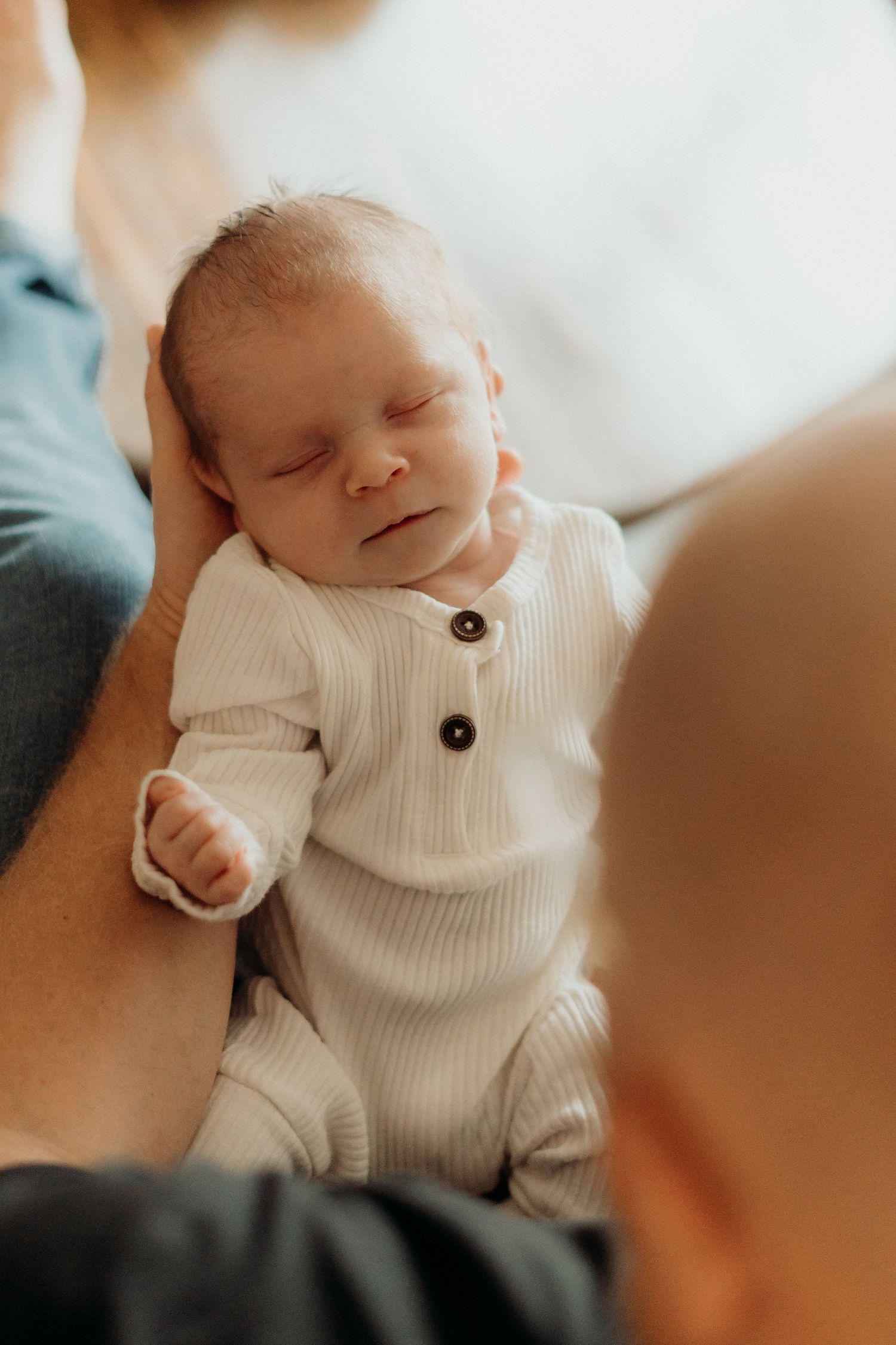 Peaceful newborn in white knit sweater smiling during naptime.