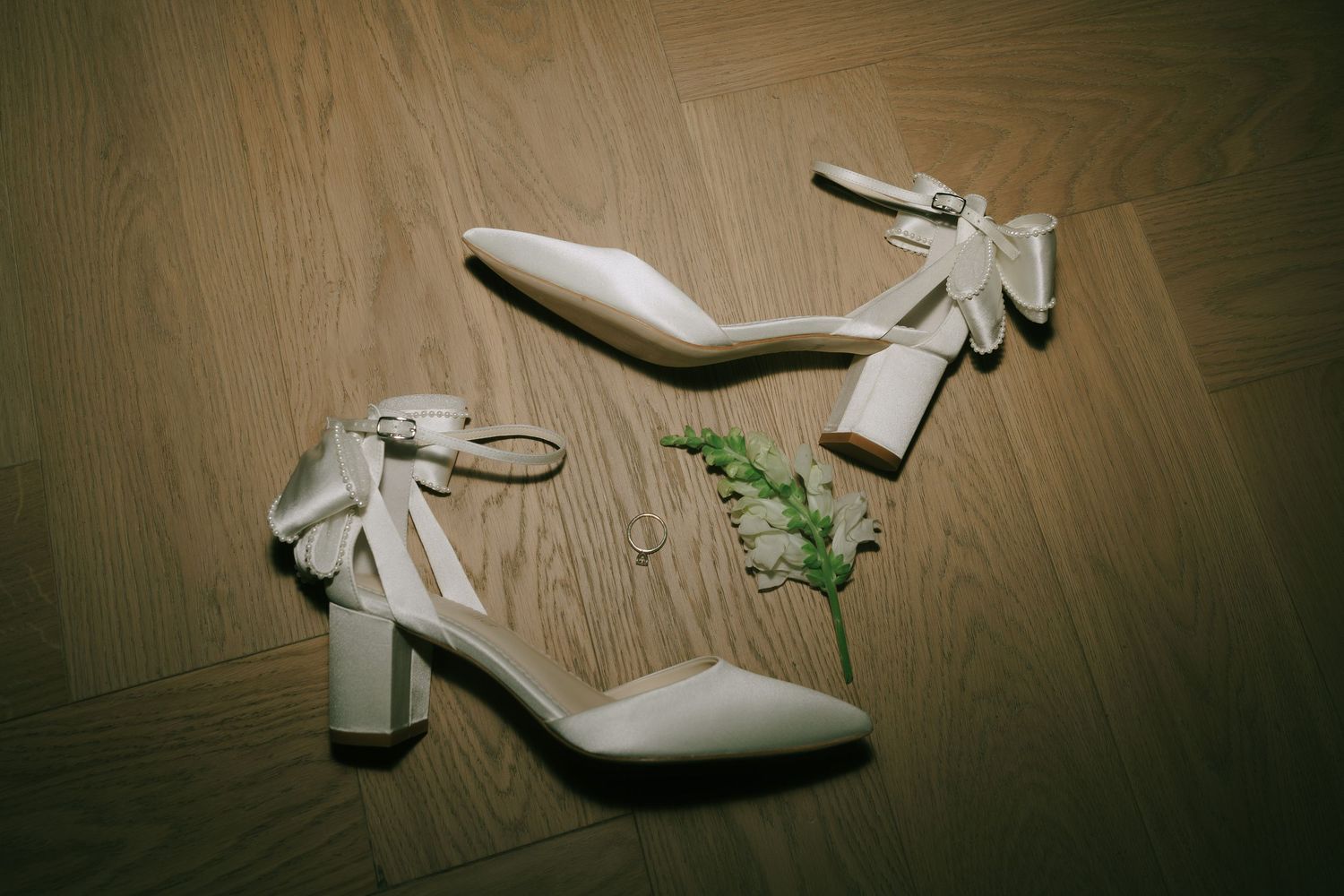 White bridal shoes scattered artistically on wooden floor with dramatic lighting.