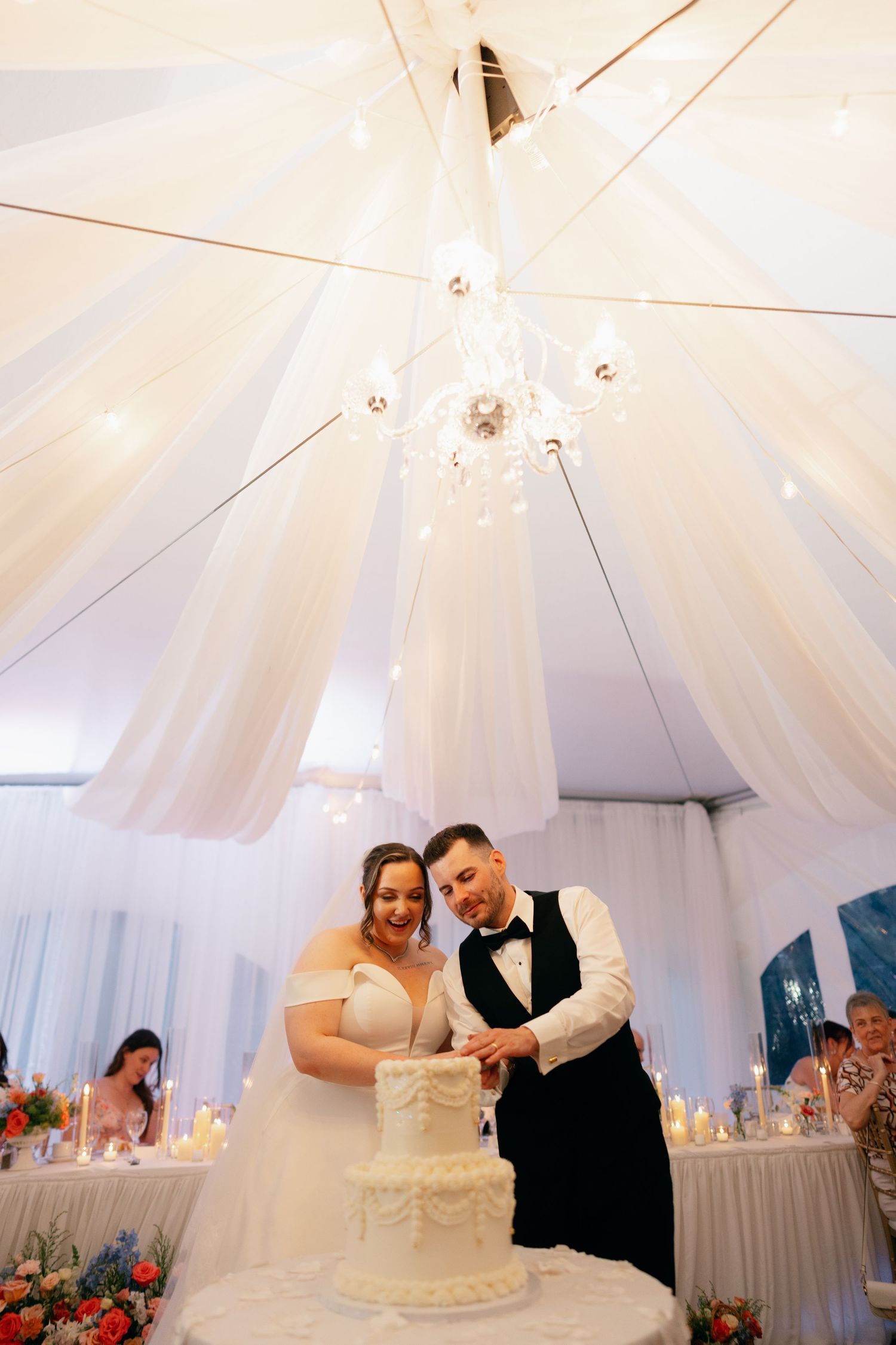 Wedding reception in a white draped tent with elegant chandelier and table settings.