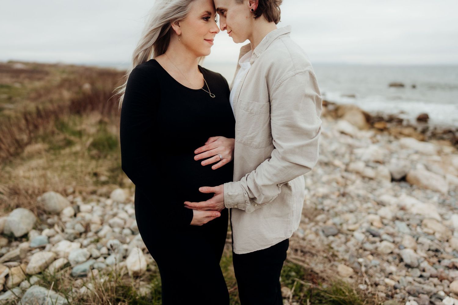 Intimate maternity portrait on a rocky coastal landscape during overcast weather.